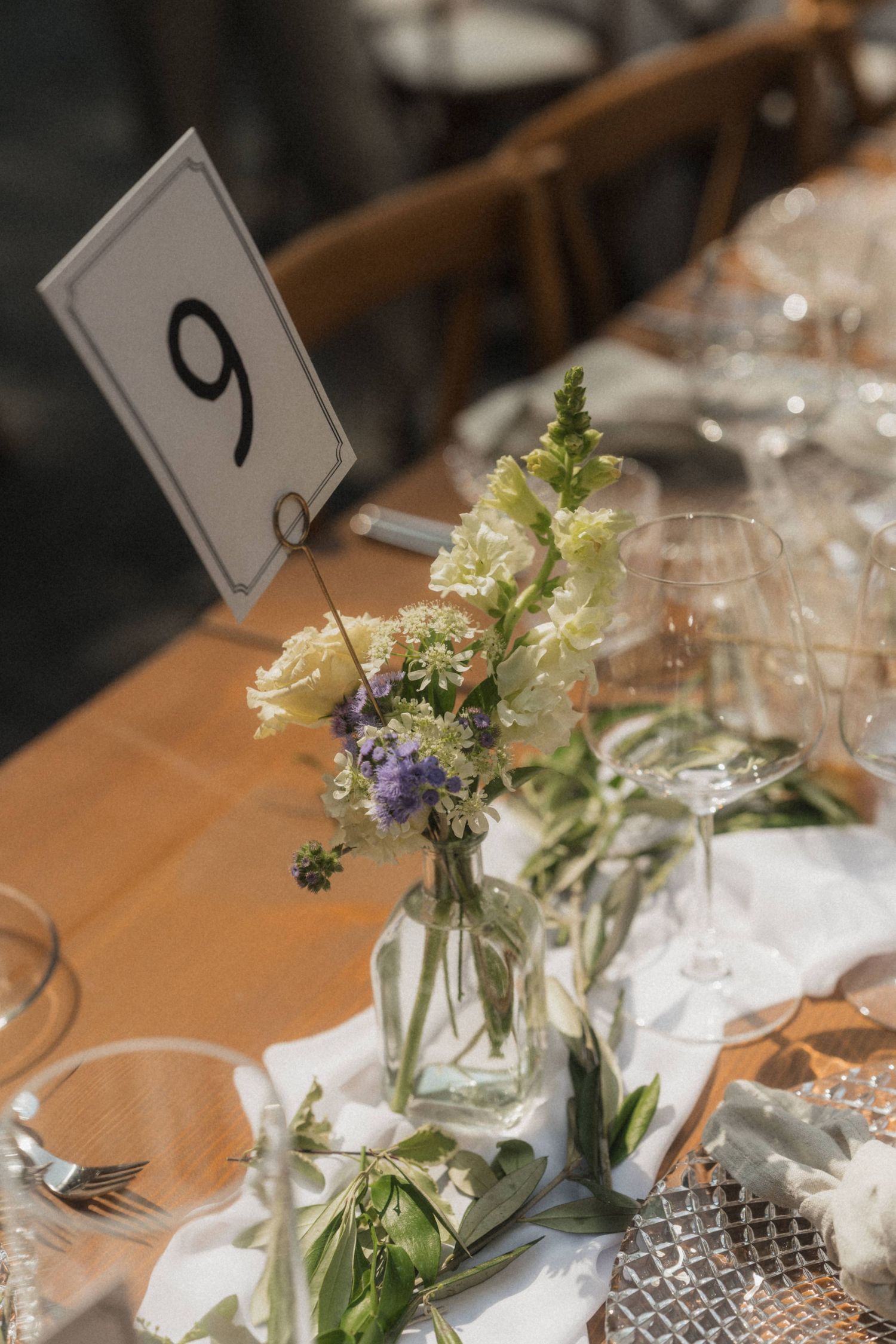 Elegant wedding table number 9 with wildflower centerpiece in glass vase and crystal glassware.
