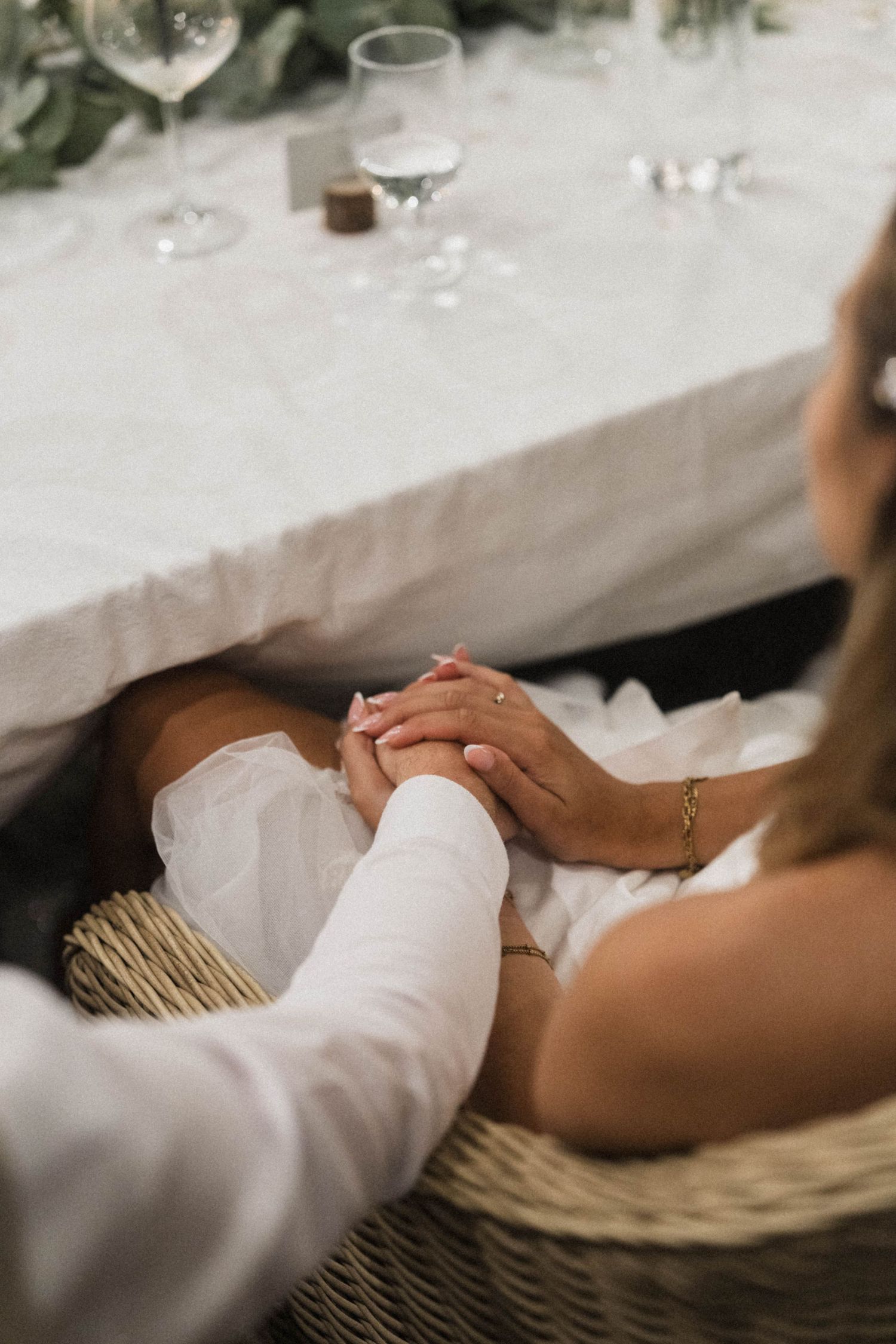 Bride and groom holding hands beneath the wedding reception table during the dinner celebration.