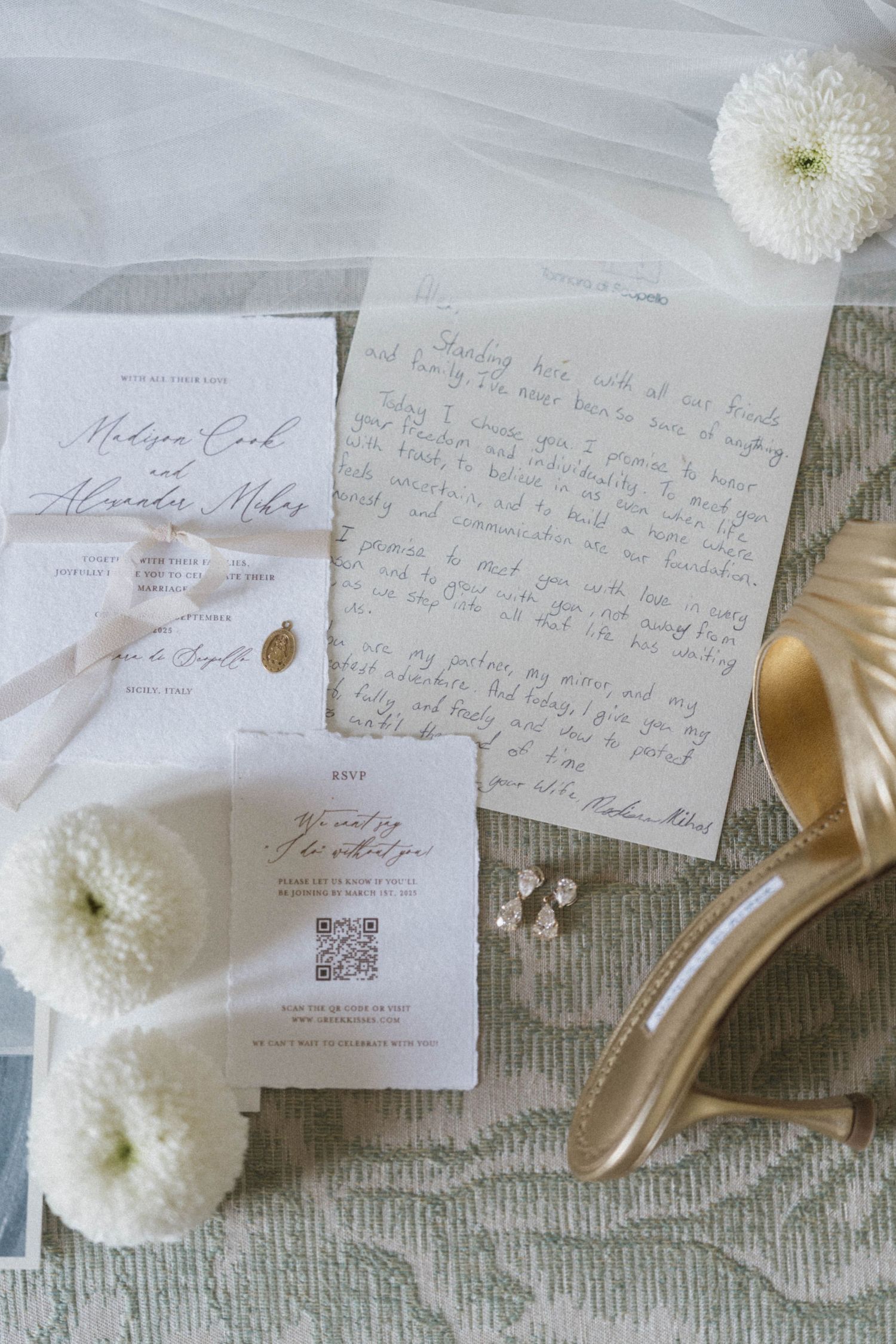 Elegant wedding stationery flat lay with handwritten vows, floral invitations, gold heels, and white flowers on sage linen.