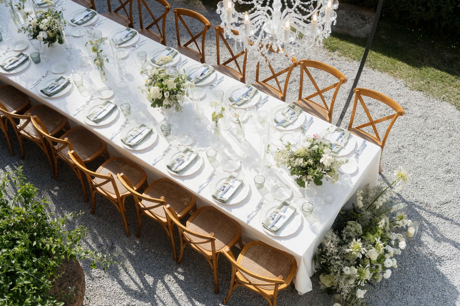 Aerial view of elegant outdoor wedding reception table with white flowers and wooden cross-back chairs.