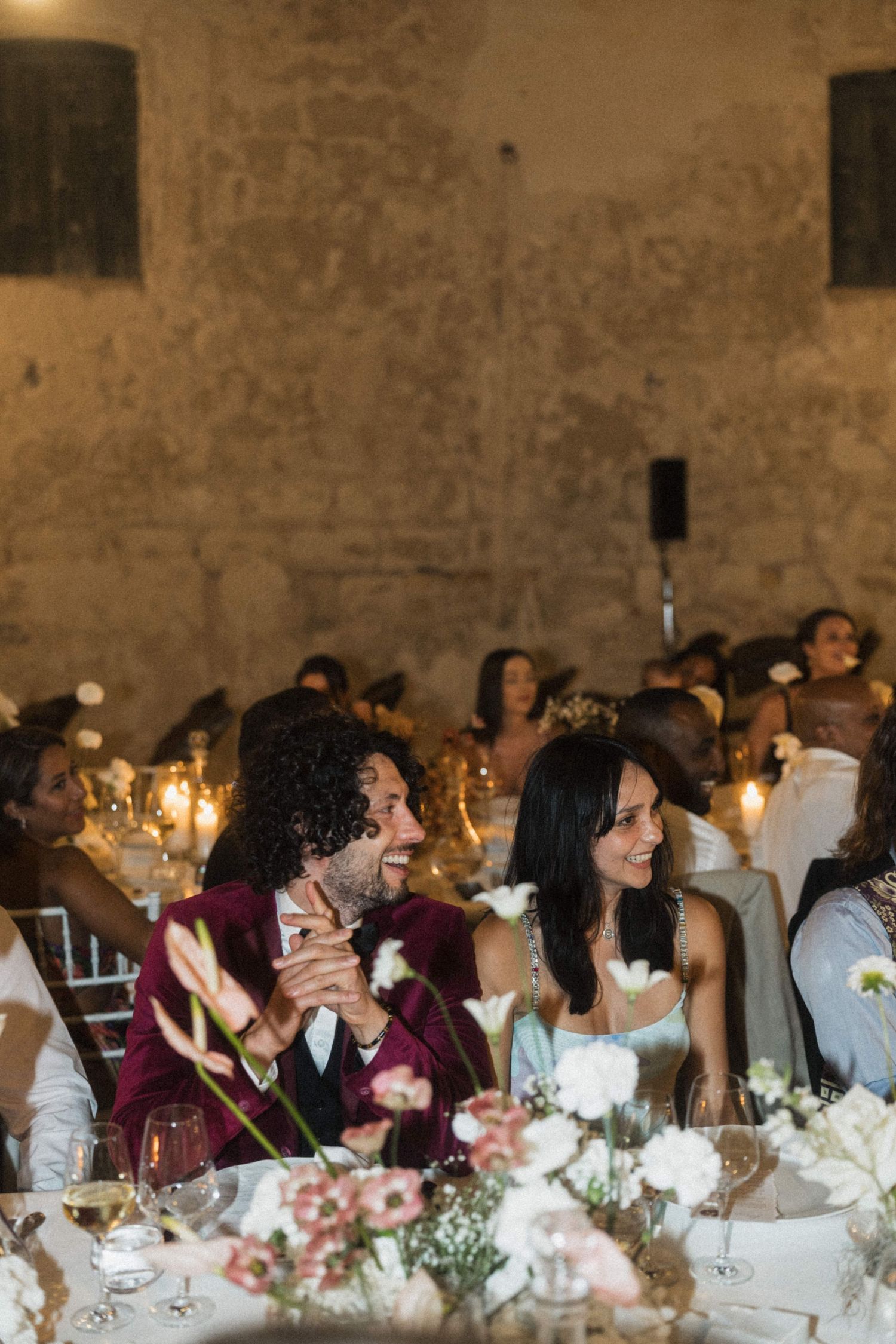Bride and groom laughing joyfully at their candlelit wedding reception table adorned with white floral arrangements.