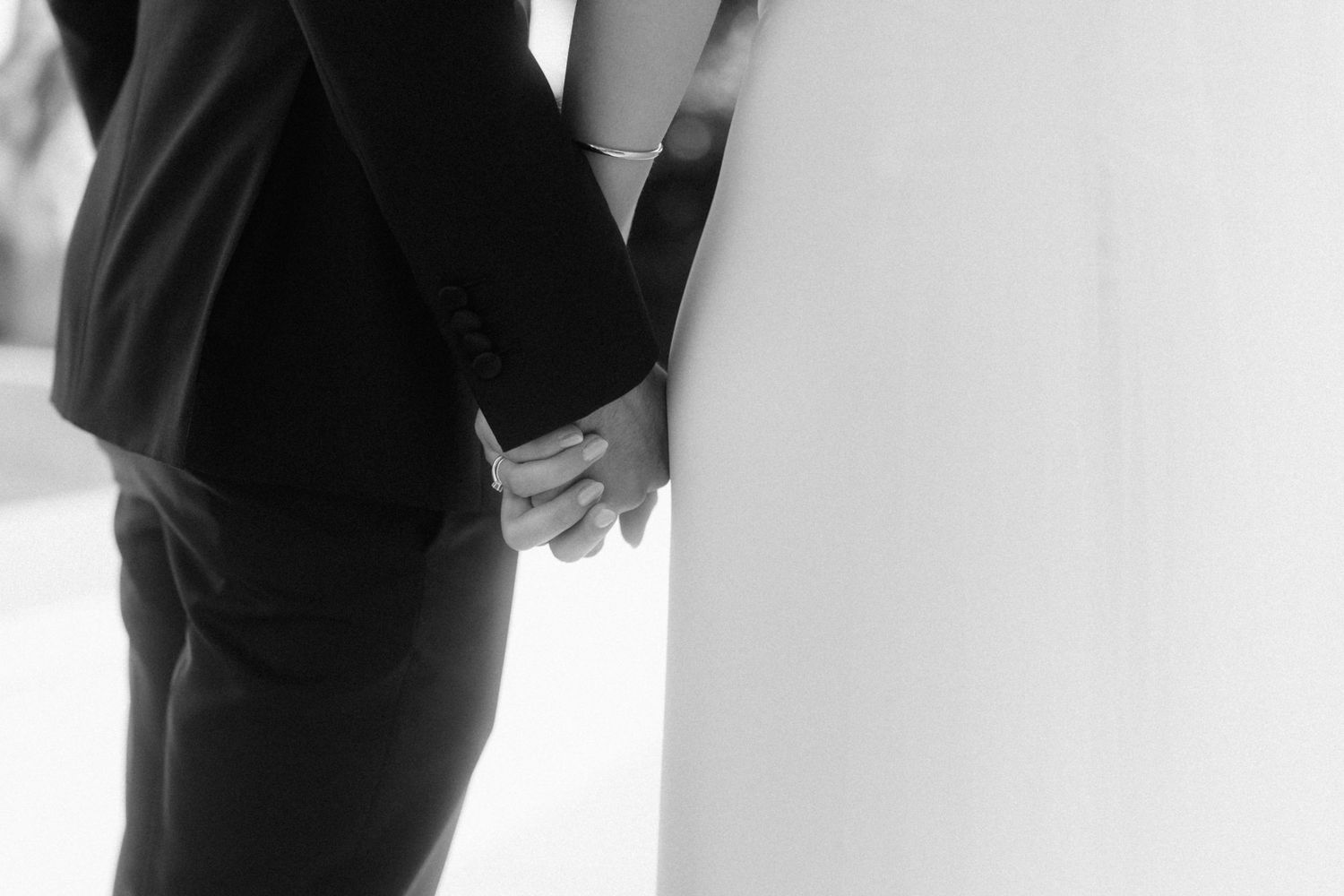 Black and white photo of bride and groom holding hands on their wedding day.