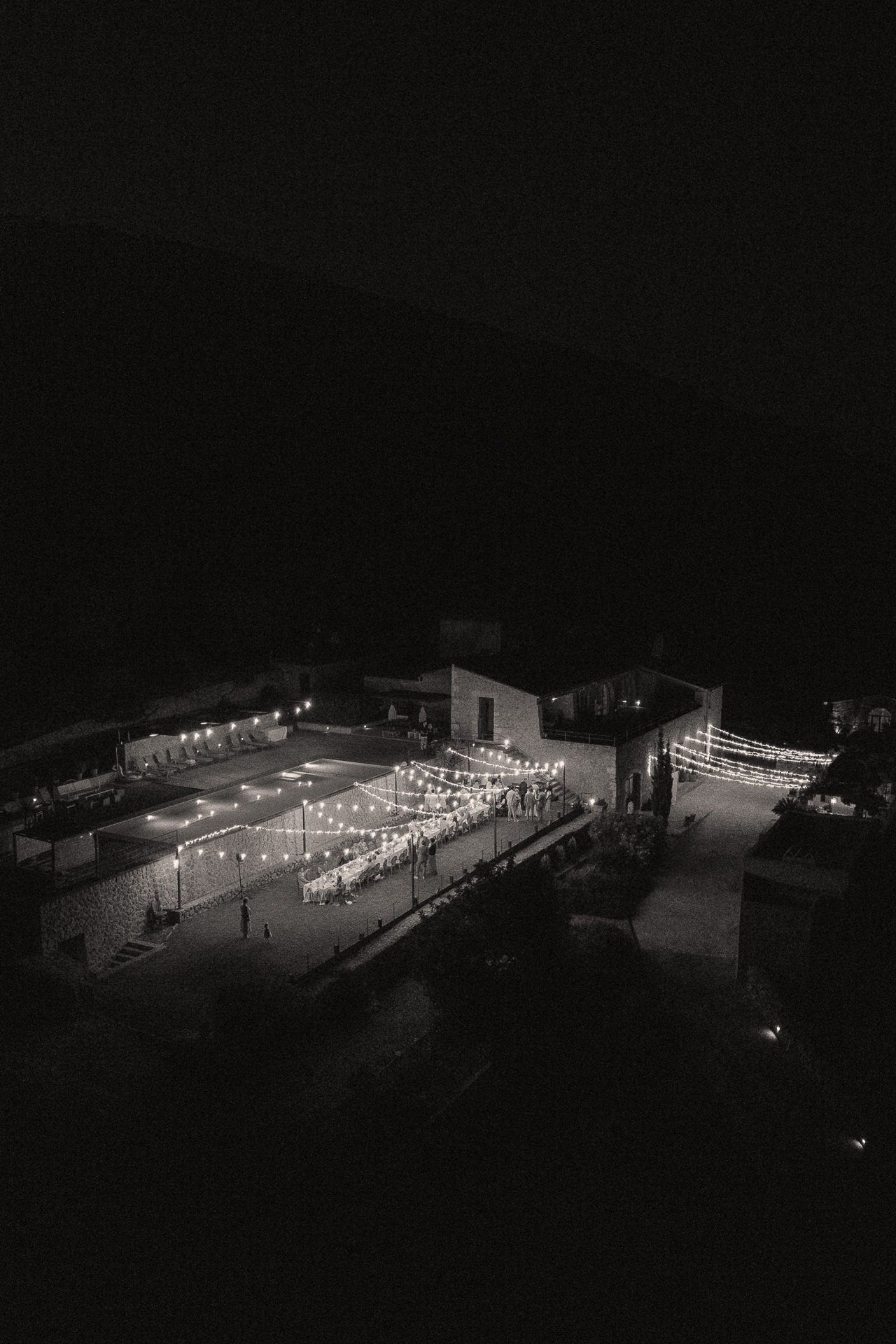 Black and white aerial night photo of an outdoor event venue illuminated by string lights.