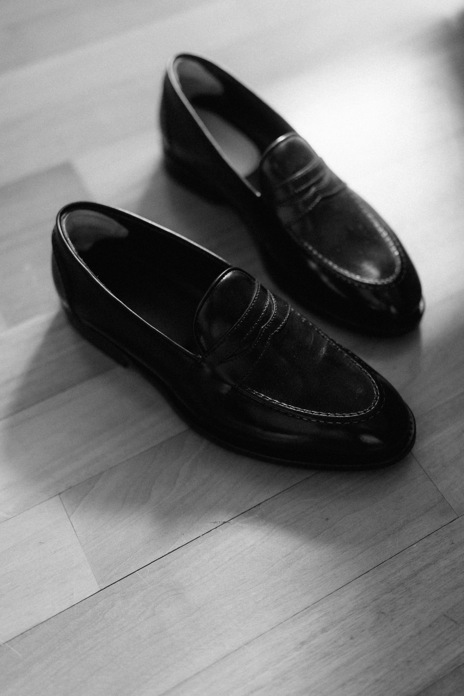 Classic black leather penny loafers on hardwood floor in elegant black and white photography.