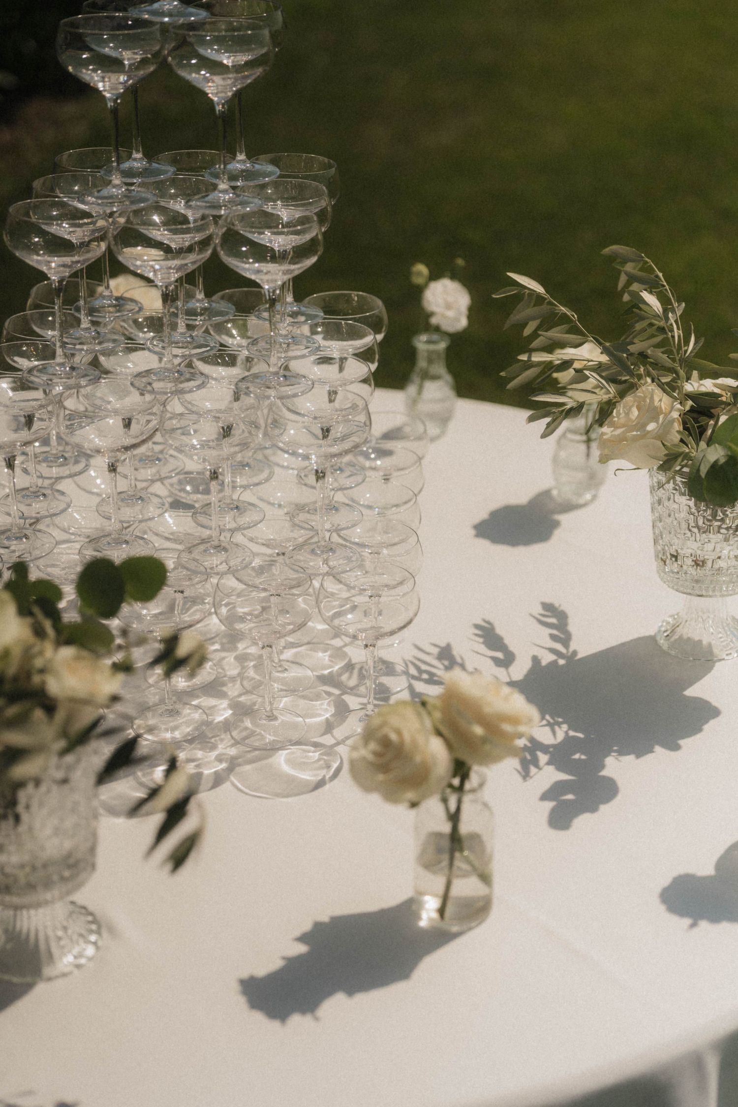 Elegant champagne tower with crystal coupe glasses and white roses on wedding reception table.