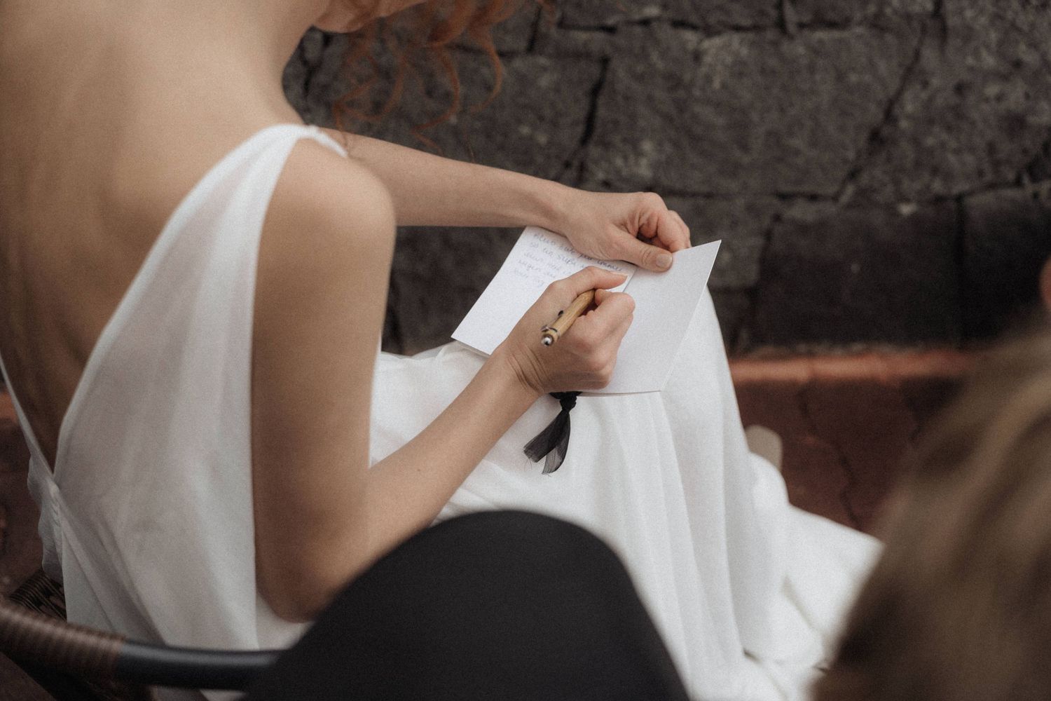 Bride in white dress writing a note while seated, captured from above in an elegant wedding setting.
