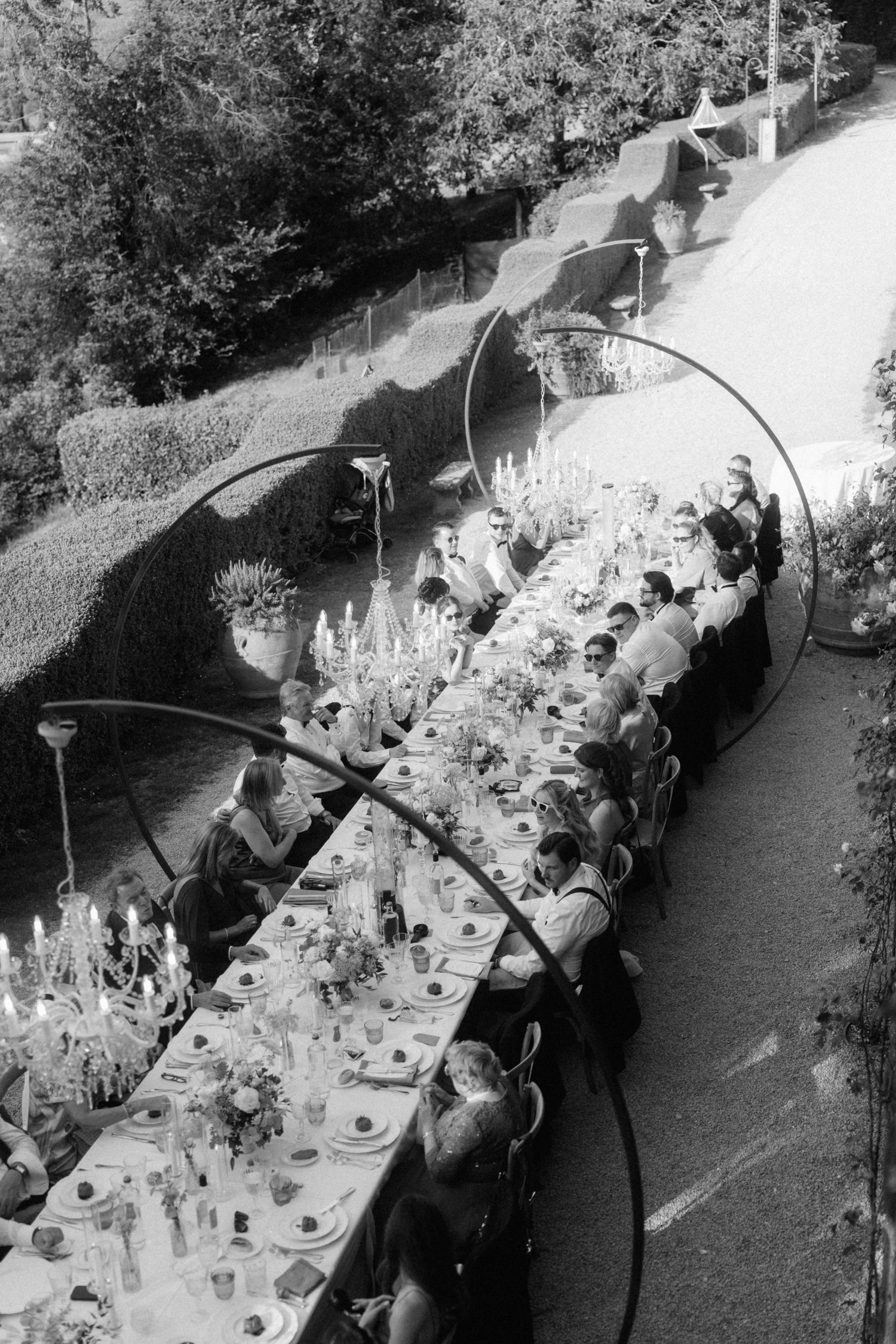 Black and white aerial view of long outdoor wedding banquet table with guests dining by candlelight.