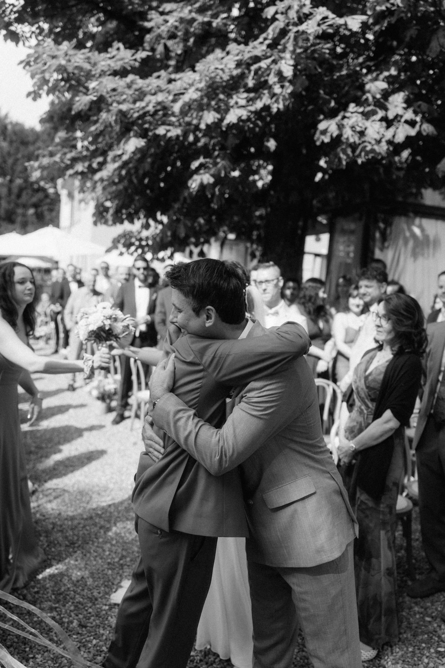 Emotional black and white photo of bride and groom embracing at outdoor wedding ceremony.