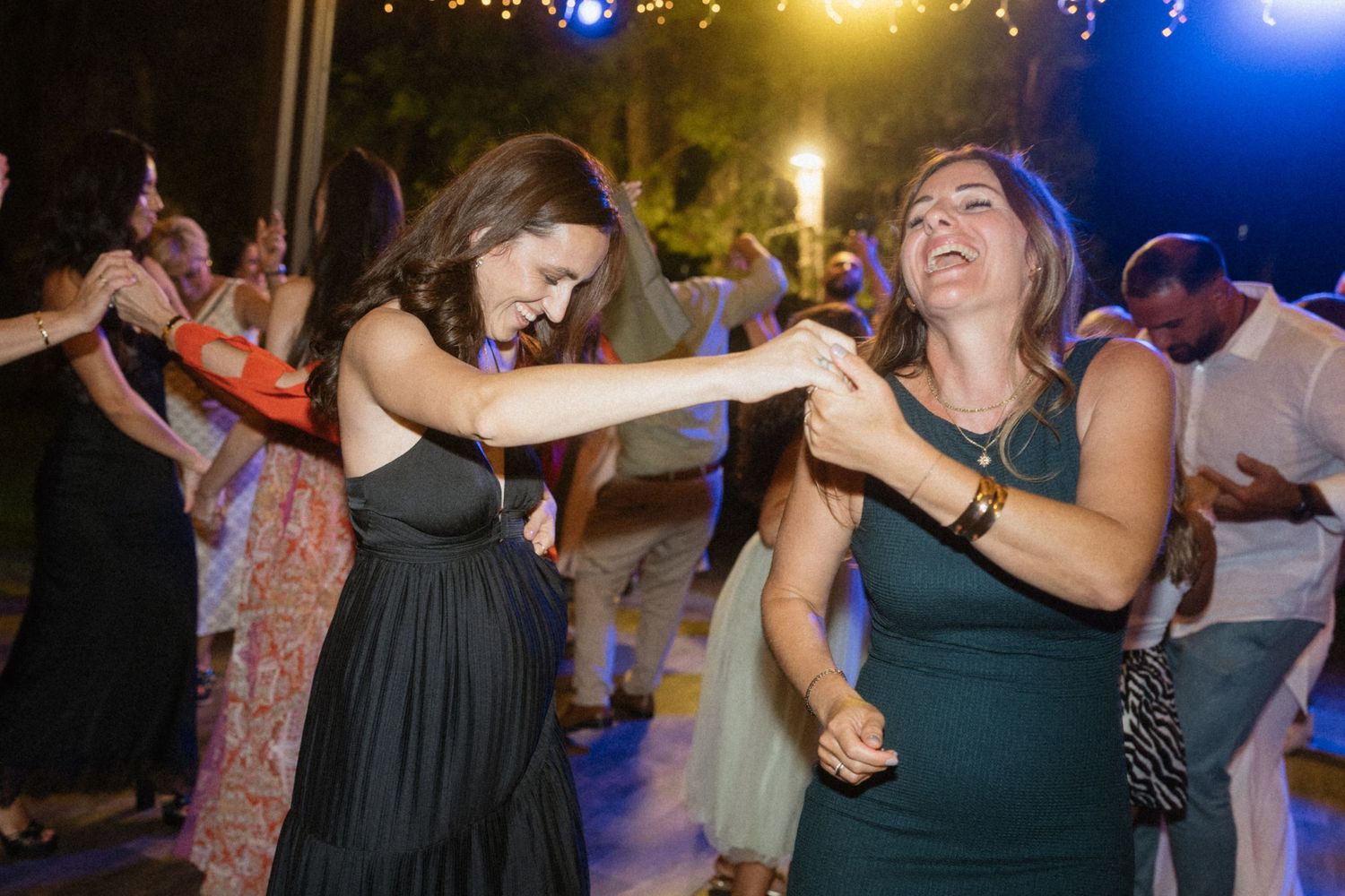 Two women dancing joyfully at an outdoor wedding reception party at night.