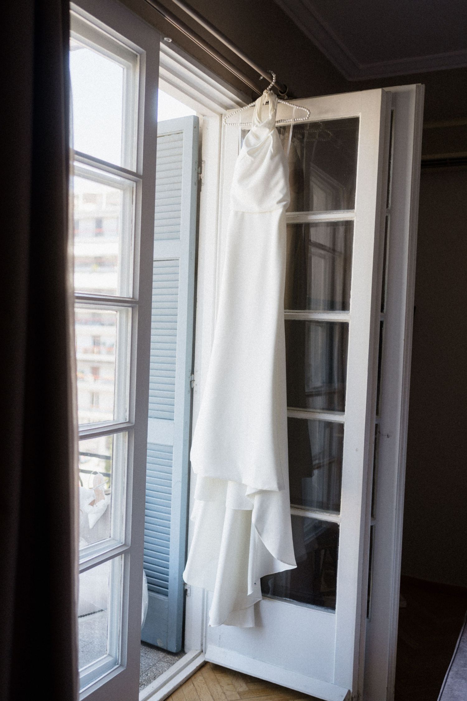 White wedding dress hanging on an open French door window in an elegant room with natural light.