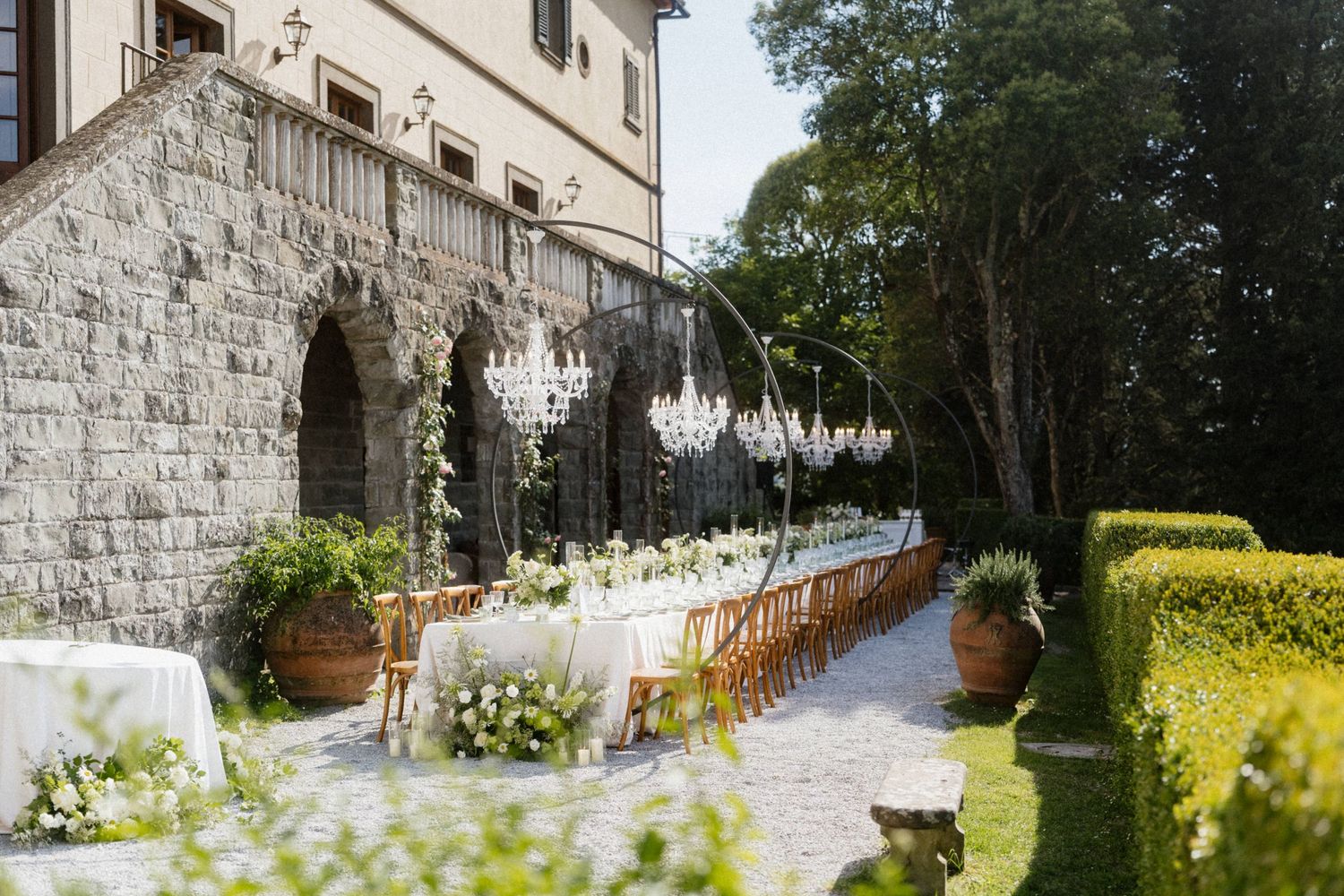 Elegant outdoor wedding reception at a Tuscan stone villa with crystal chandeliers and white floral arrangements.