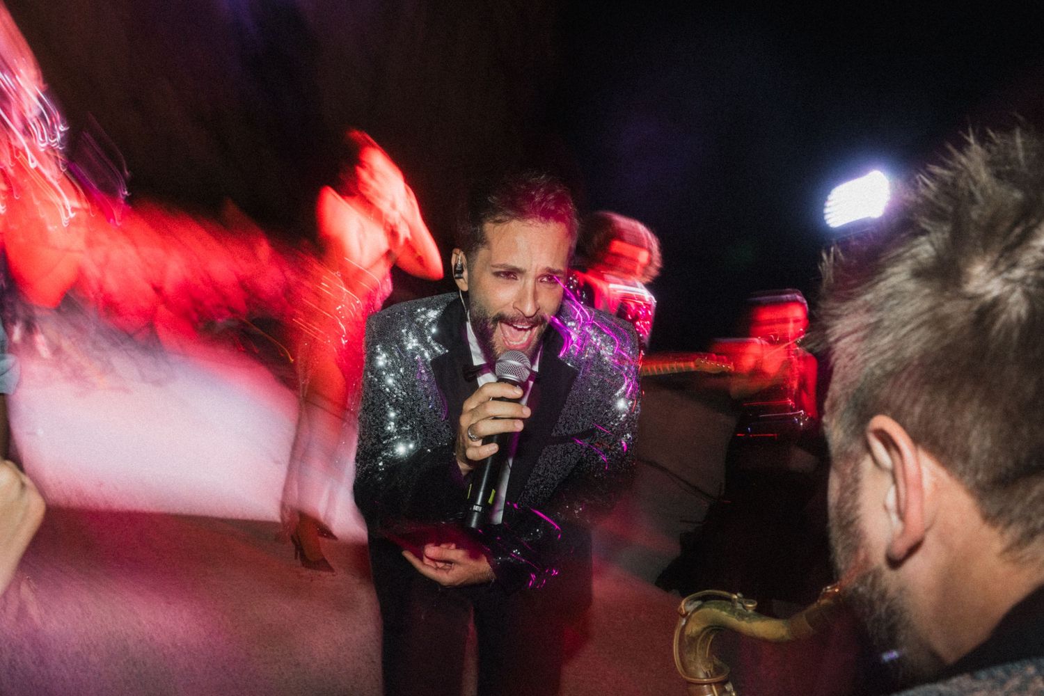 Male performer in sequin jacket singing into microphone at lively wedding reception party.
