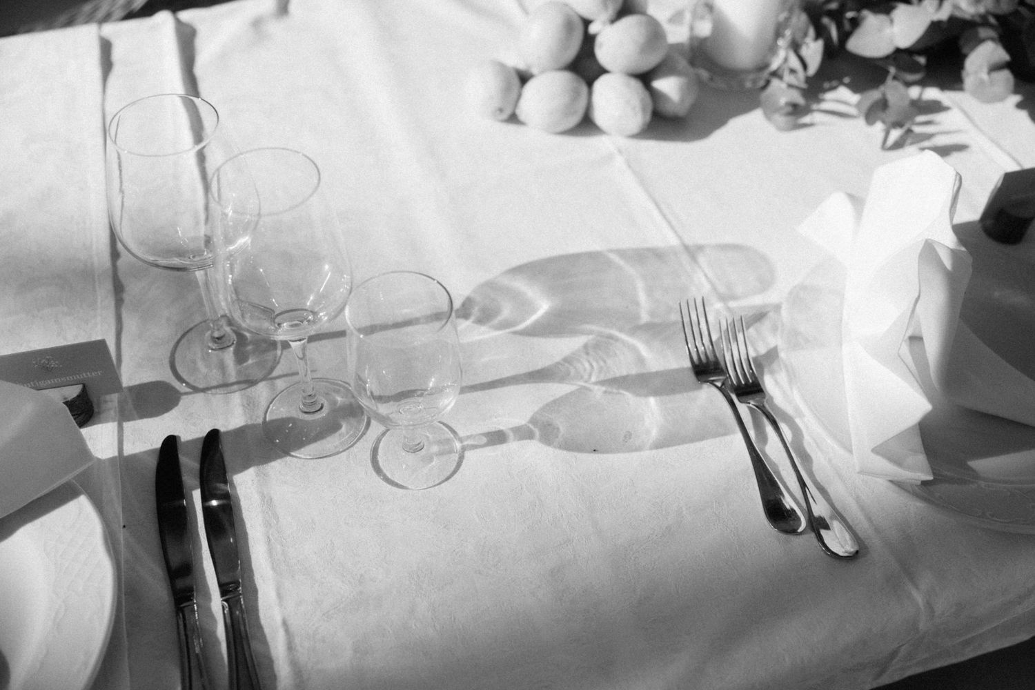 Black and white close-up of elegant wedding table setting with wine glasses and silverware.