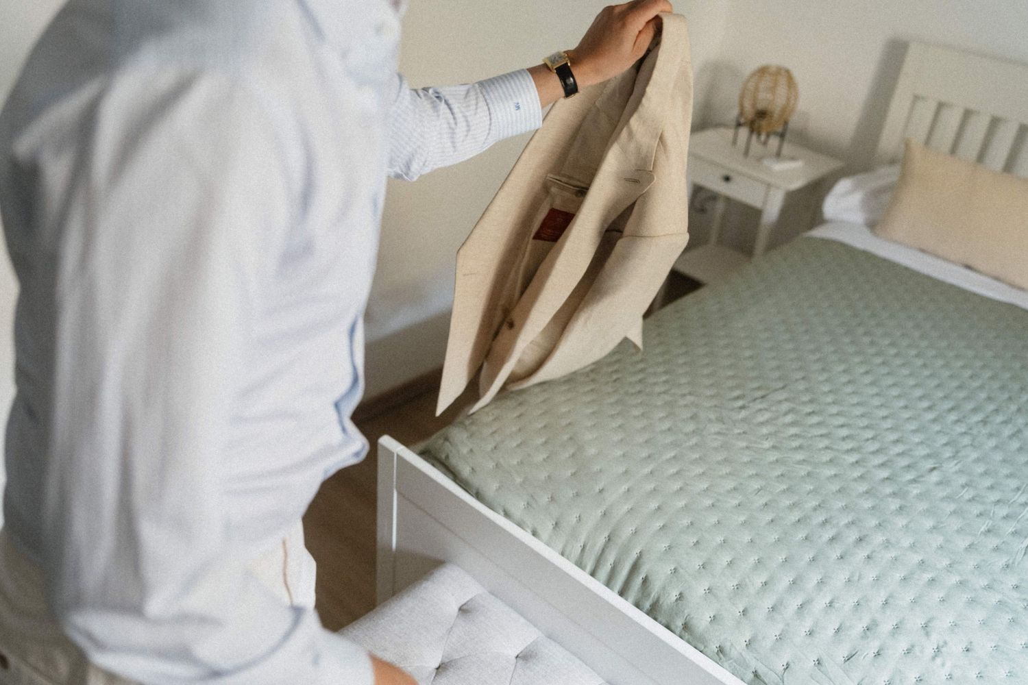Person placing a pillow into a white pillowcase on a bed with a light green mattress in a bright bedroom.