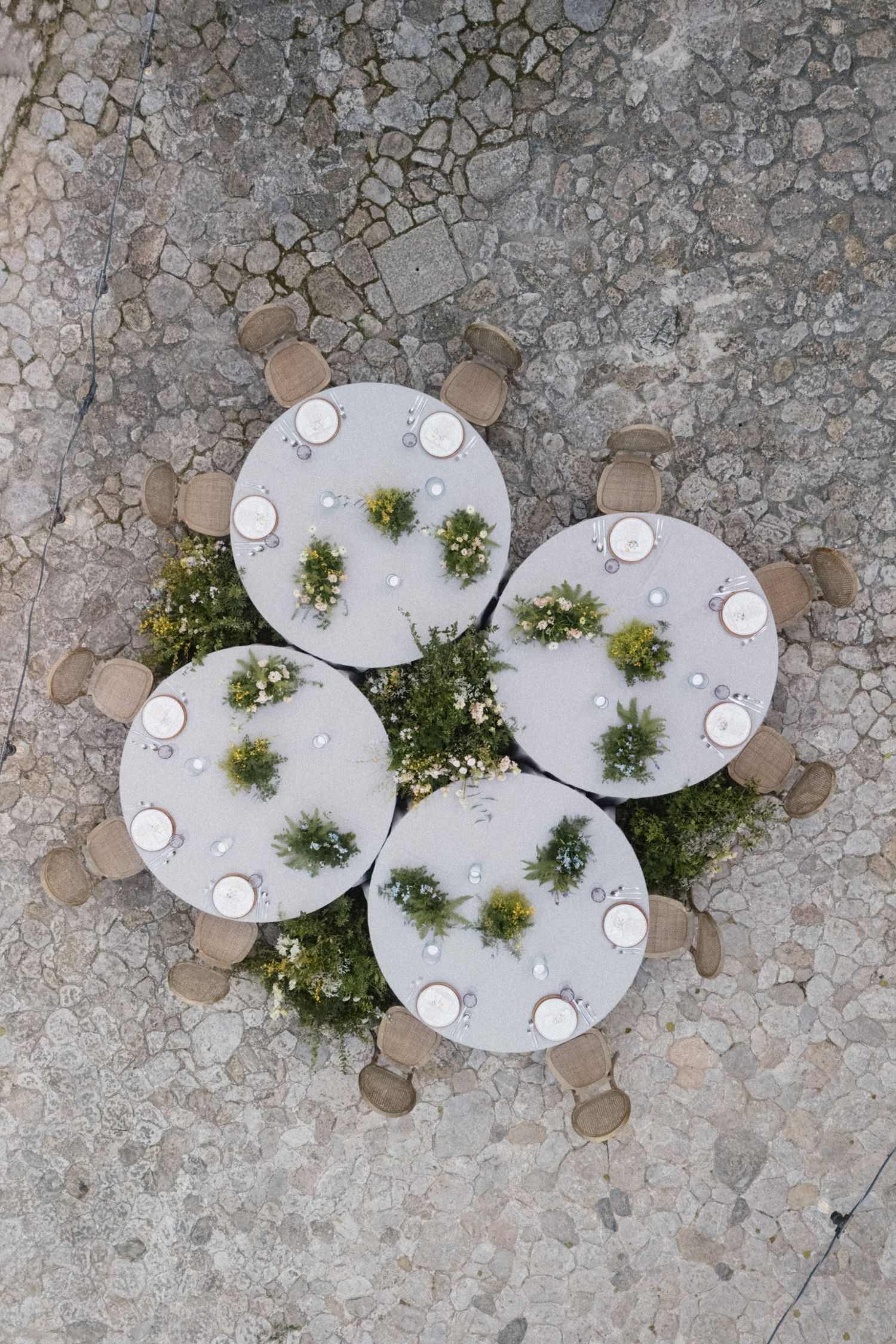 Aerial view of round wedding reception tables with lush green centerpieces on cobblestone venue.