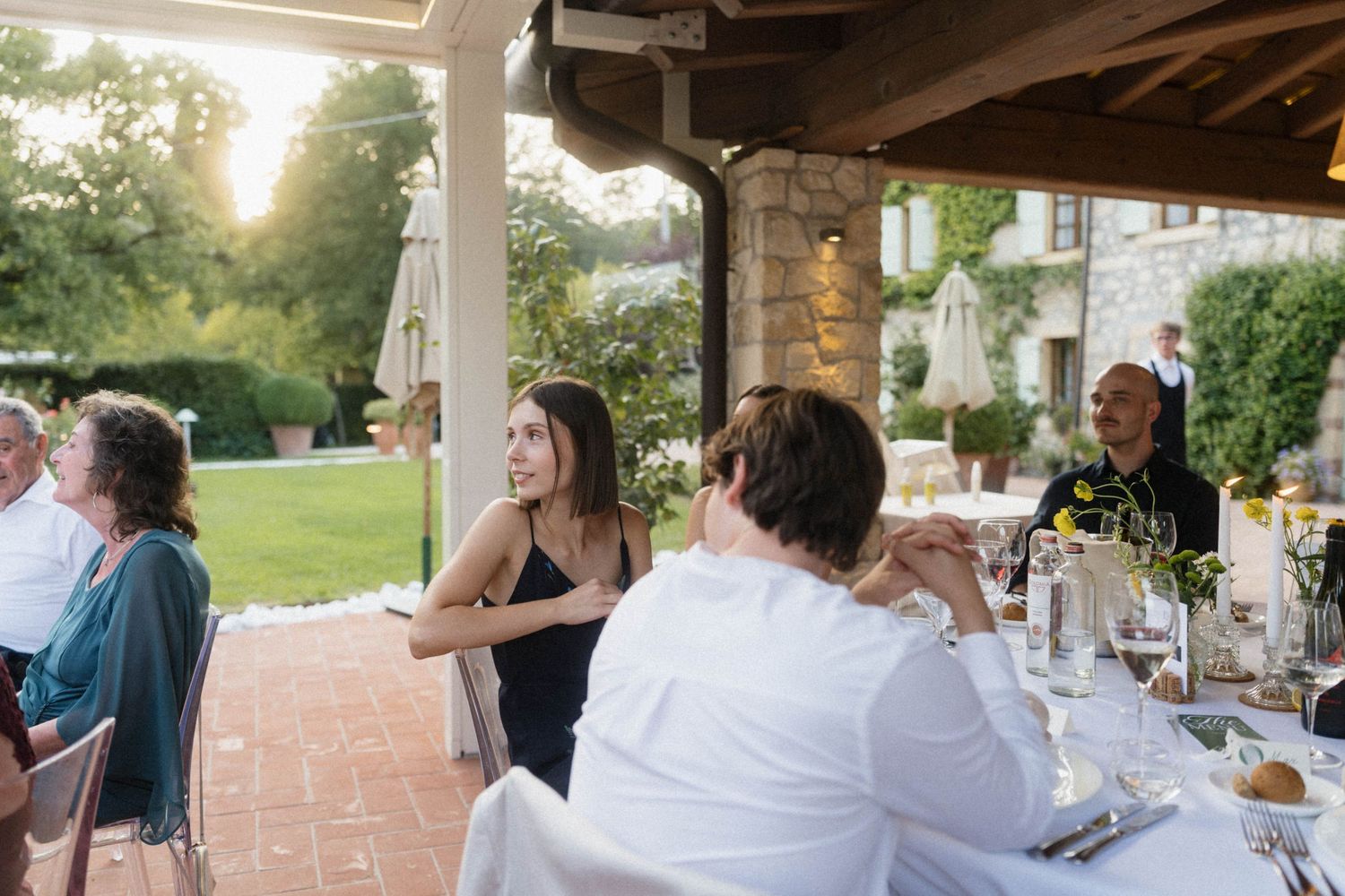 Guests socializing at an outdoor wedding reception dinner on a patio at golden hour.