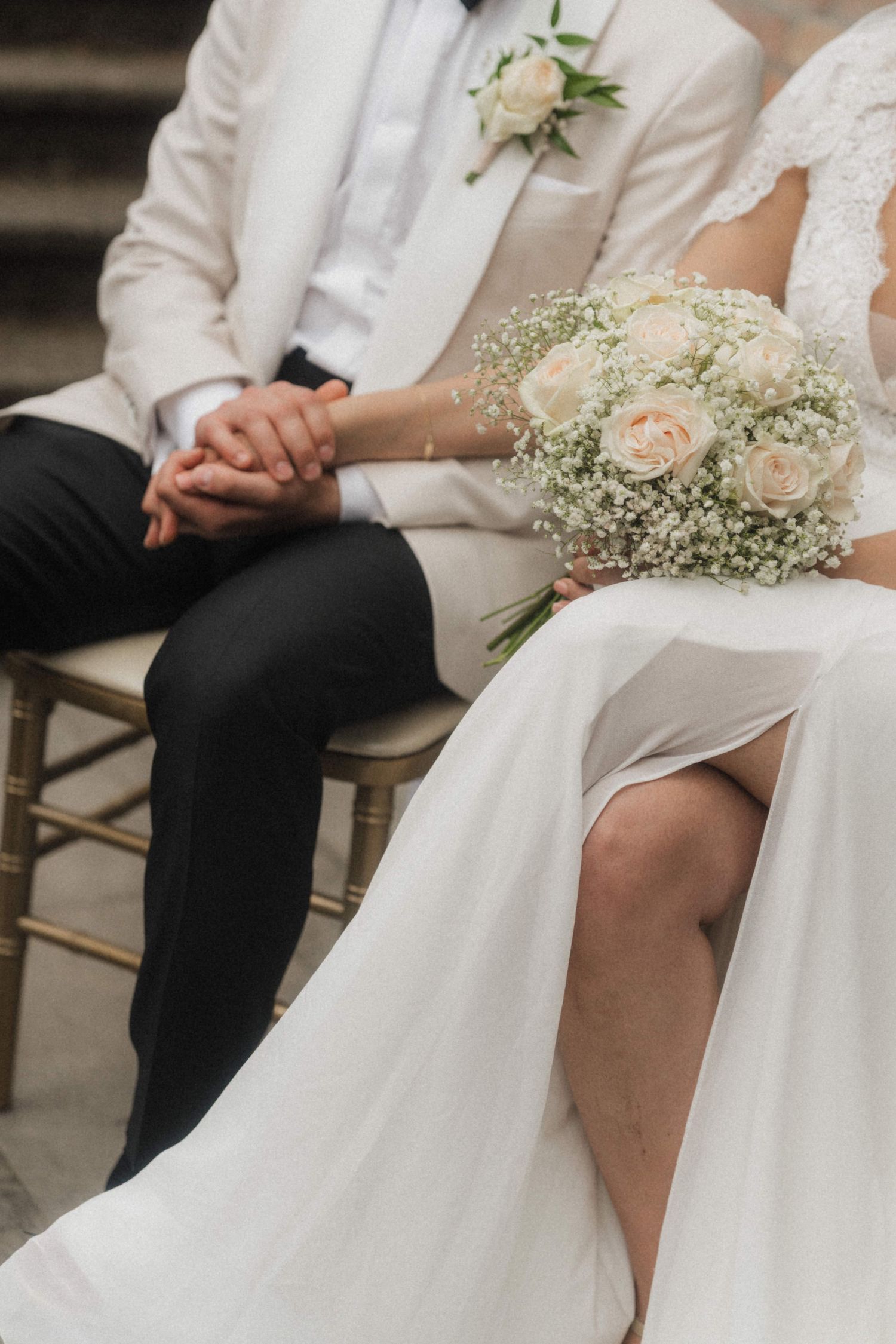Close-up of bride and groom holding hands, bride holding white rose and baby's breath bouquet.