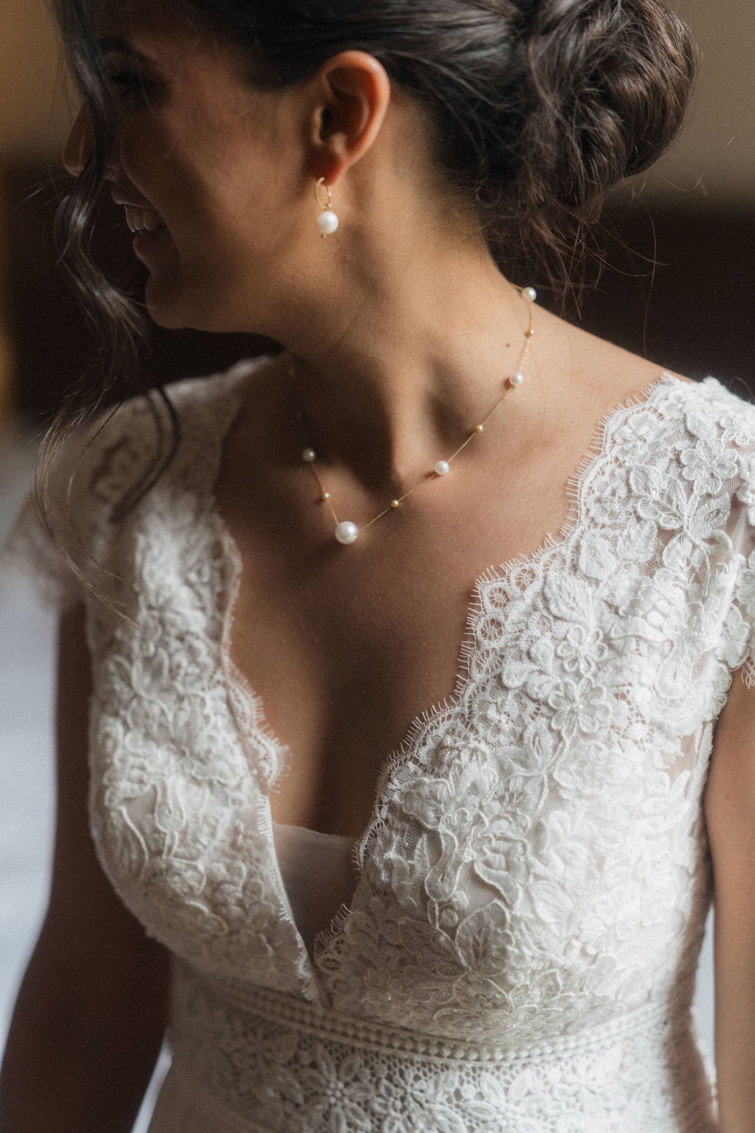 Close-up of bride wearing lace V-back wedding dress with delicate pearl necklace and matching earrings.