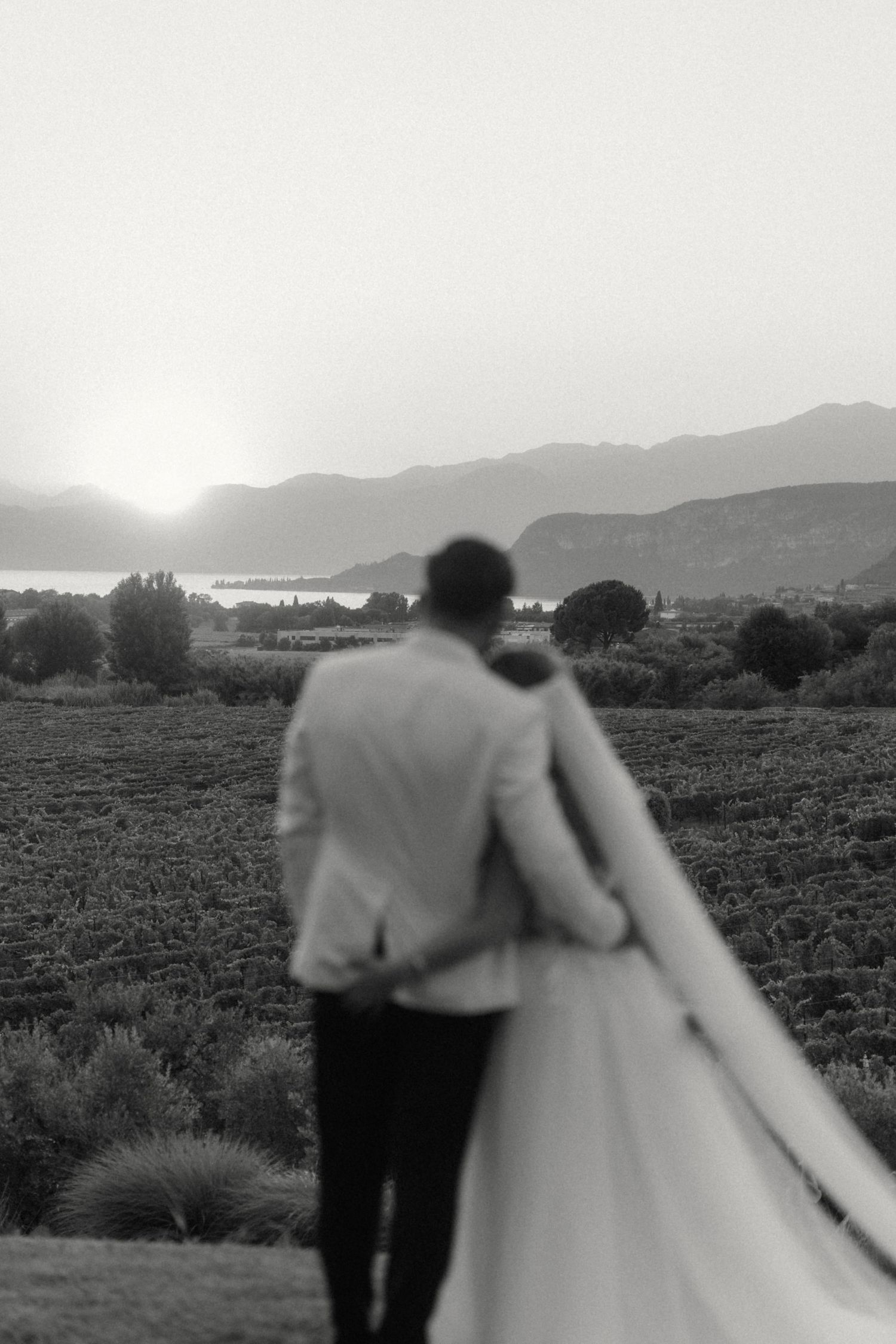 Black and white photo of a bride and groom embracing while overlooking a scenic mountain lake at sunset.