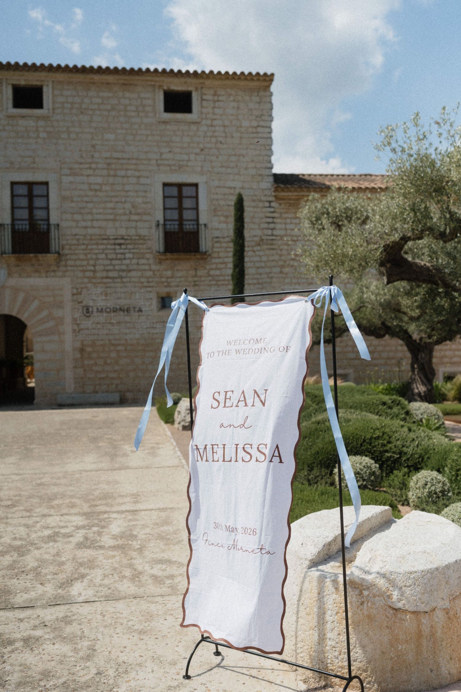 Wedding welcome sign for Sean and Melissa displayed on a stand outside a rustic stone venue.