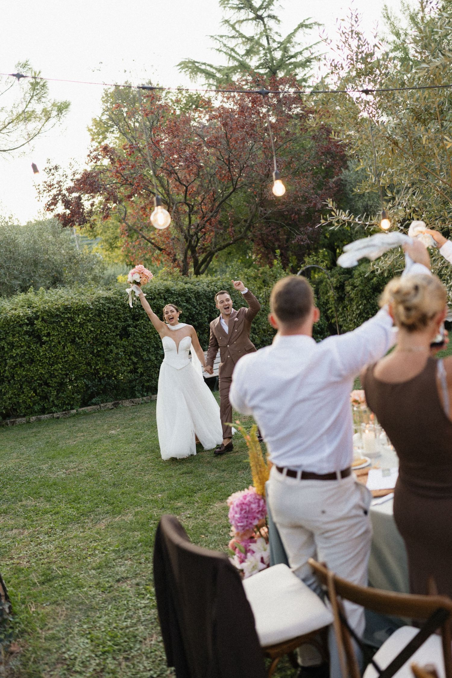 Bride and groom making a joyful entrance at their outdoor garden wedding reception with cheering guests.