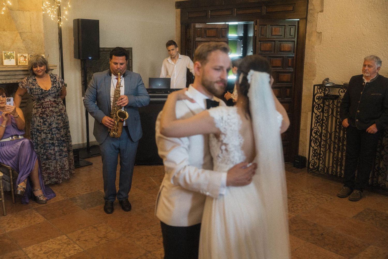 Bride and groom share their first dance while a saxophonist performs at their wedding reception.