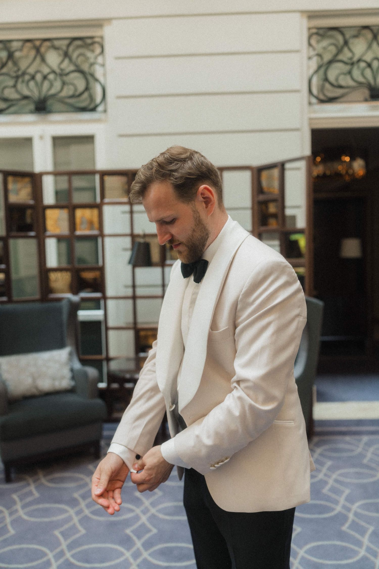 Groom in white tuxedo jacket and black bow tie adjusting cufflinks before wedding ceremony.