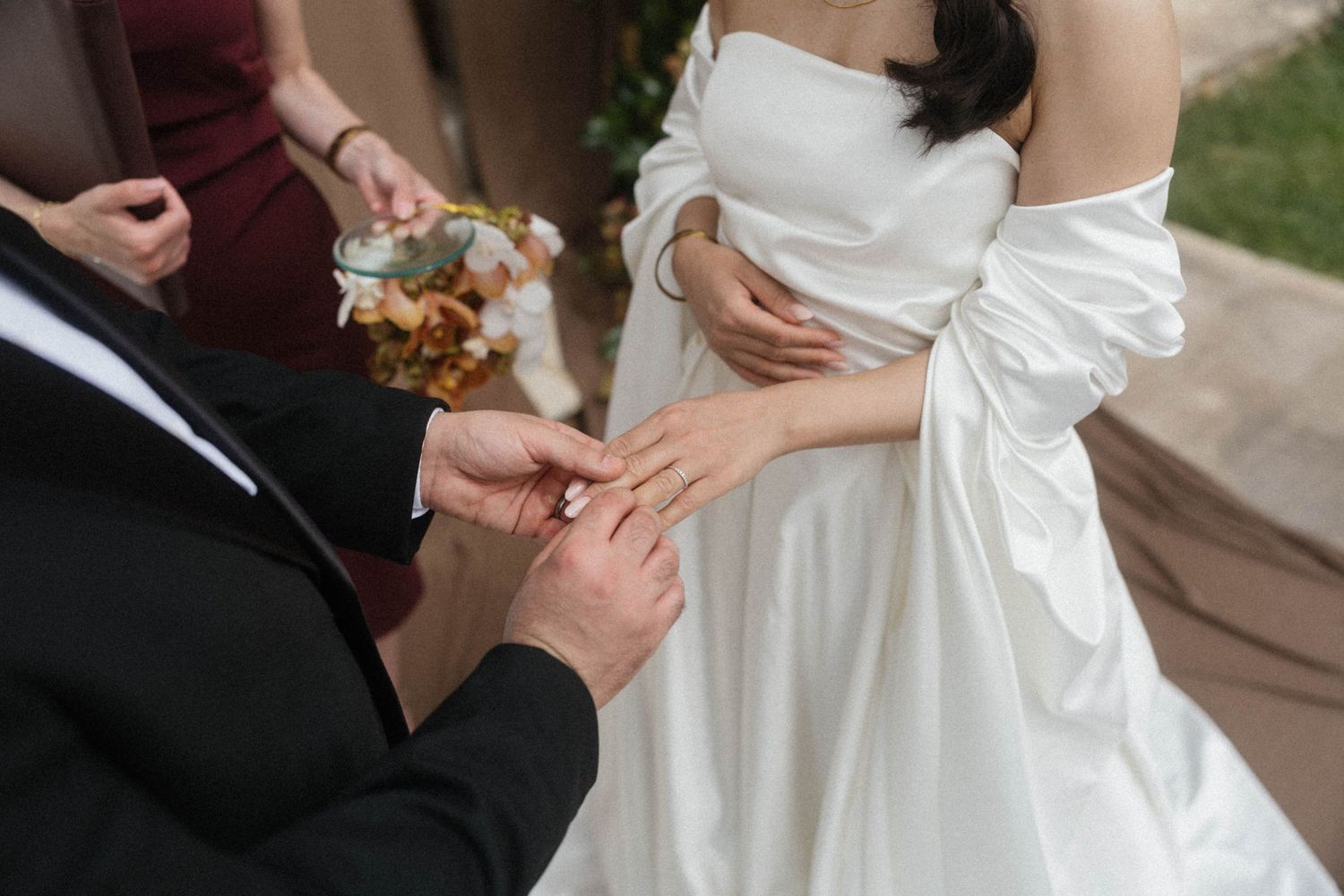 Groom placing a gold wedding ring on the bride's finger during outdoor ceremony.