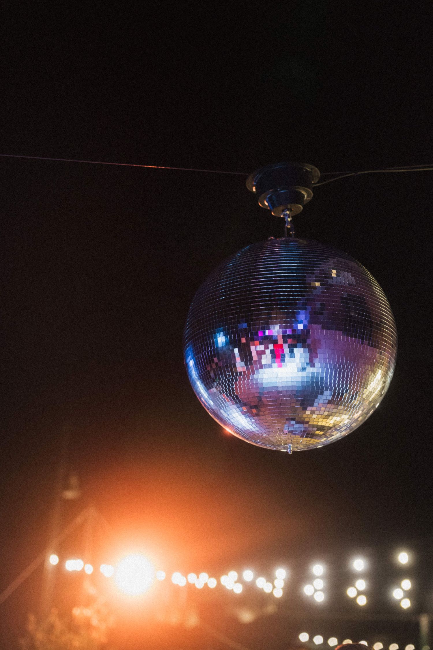 Sparkling disco ball hanging against dark night sky with bokeh lights glowing in background.