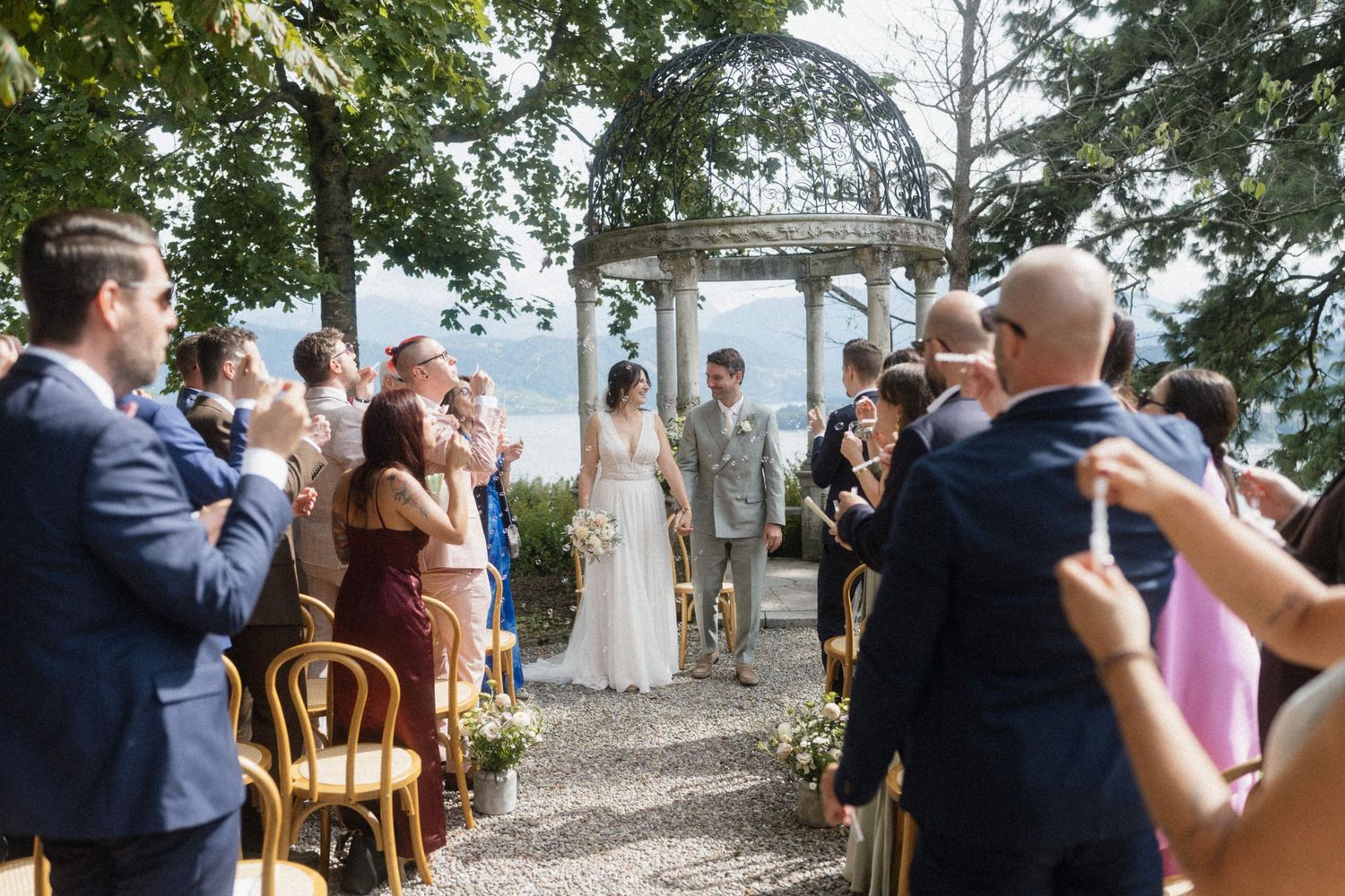 Guests applaud as bride and groom stand at altar of outdoor lakeside wedding.