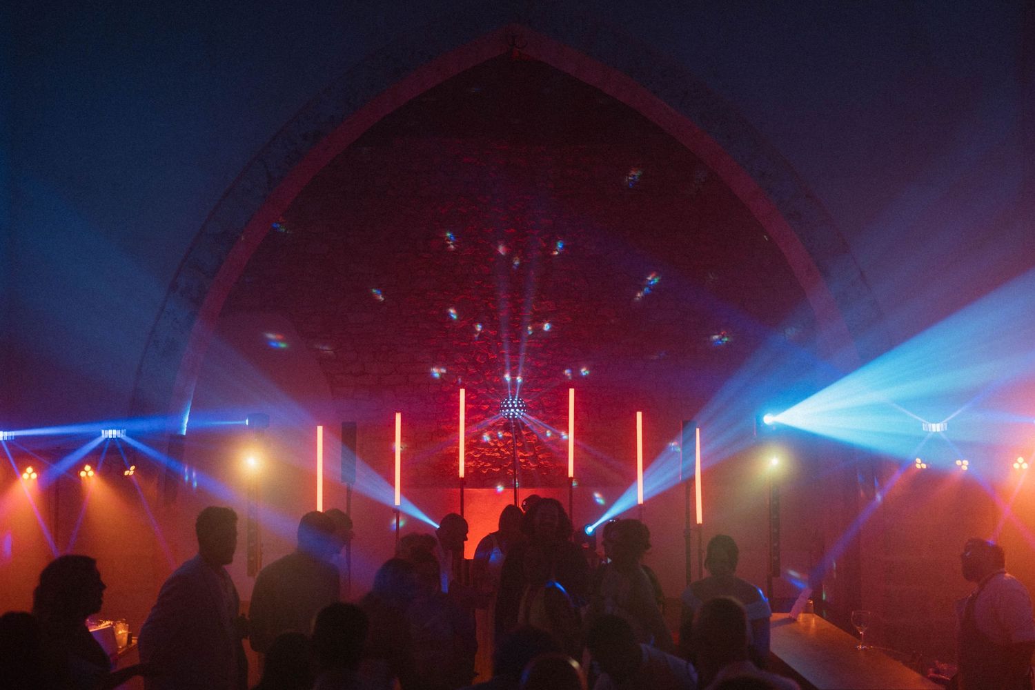 Vibrant nightclub interior with colorful laser lights illuminating a packed dance floor under an arched ceiling.