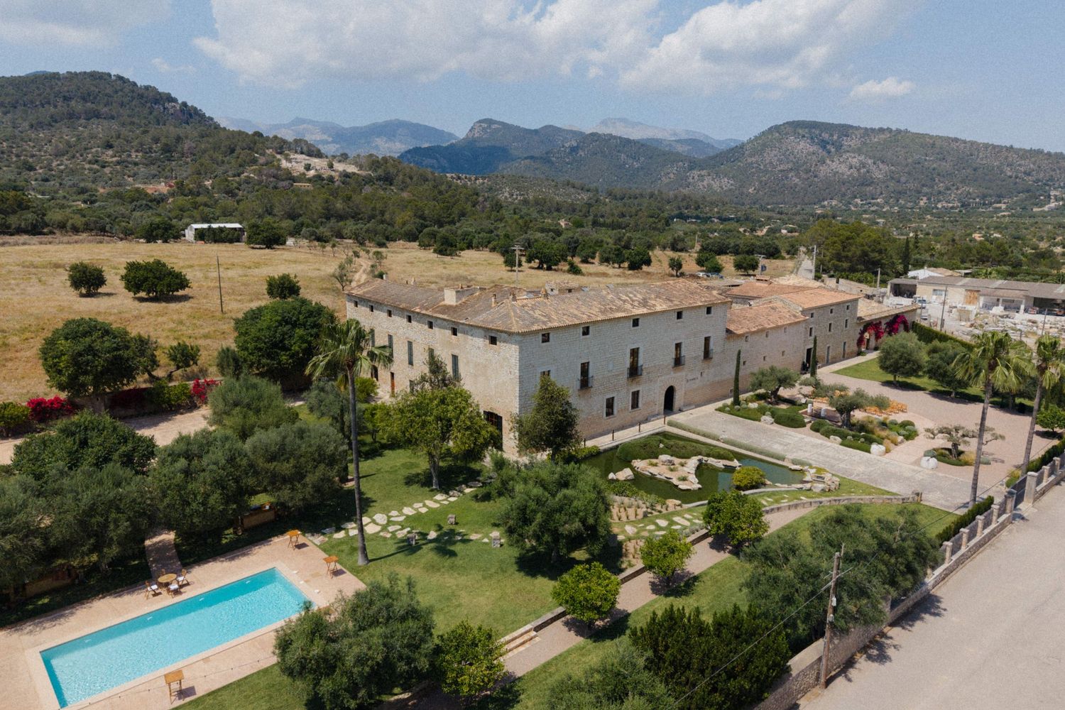 Aerial view of a large stone country estate with pool, manicured gardens, and mountain backdrop in Mallorca.