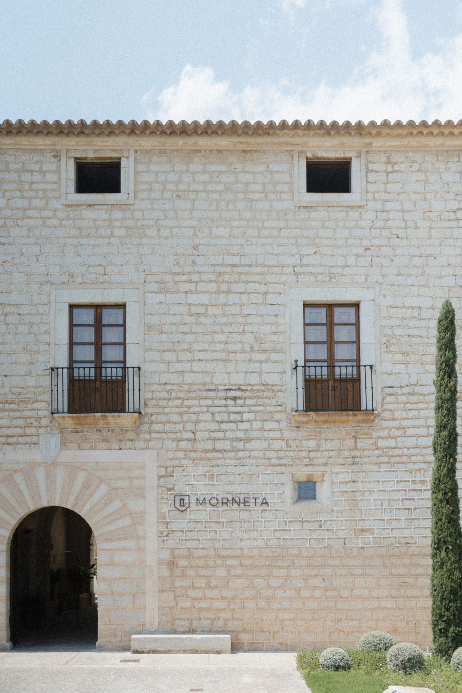 Historic stone building facade of Morneta with arched entrance, wooden balconies, and terracotta roof tiles.