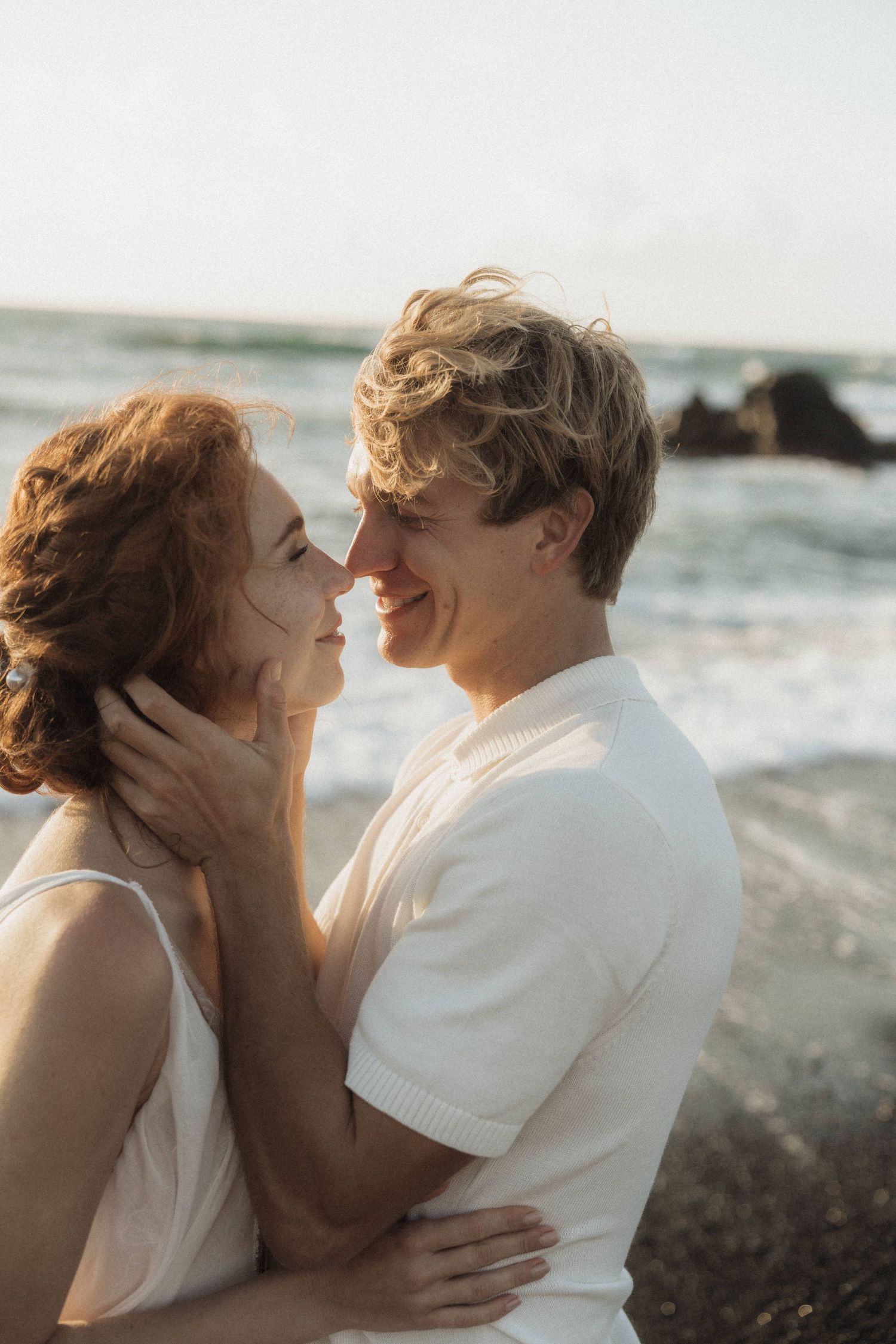 Smiling couple sharing a romantic moment on a black sand beach at golden hour.