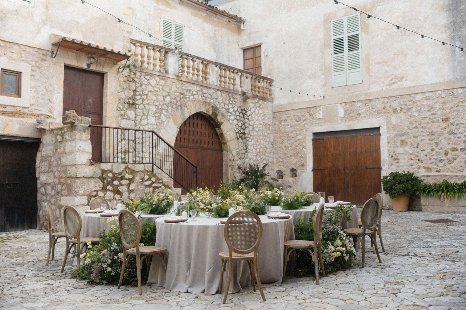 Elegant outdoor wedding reception table set in a rustic stone cobblestone courtyard with lush floral centerpieces.