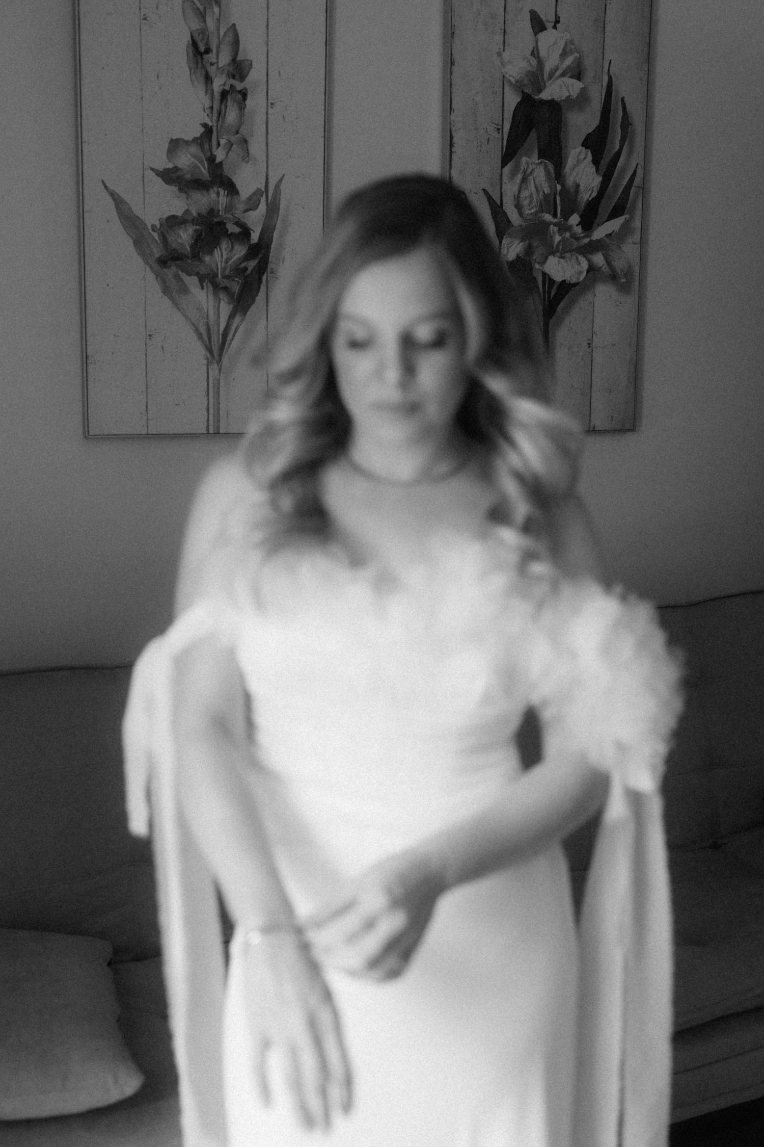 Soft focus portrait of a blonde bride in a white wedding dress with feathered sleeves looking down.