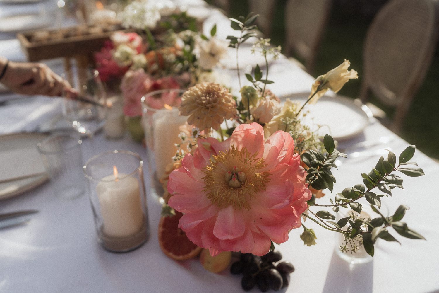 Pink peony and wildflower centerpiece with candles on a white linen wedding reception table.