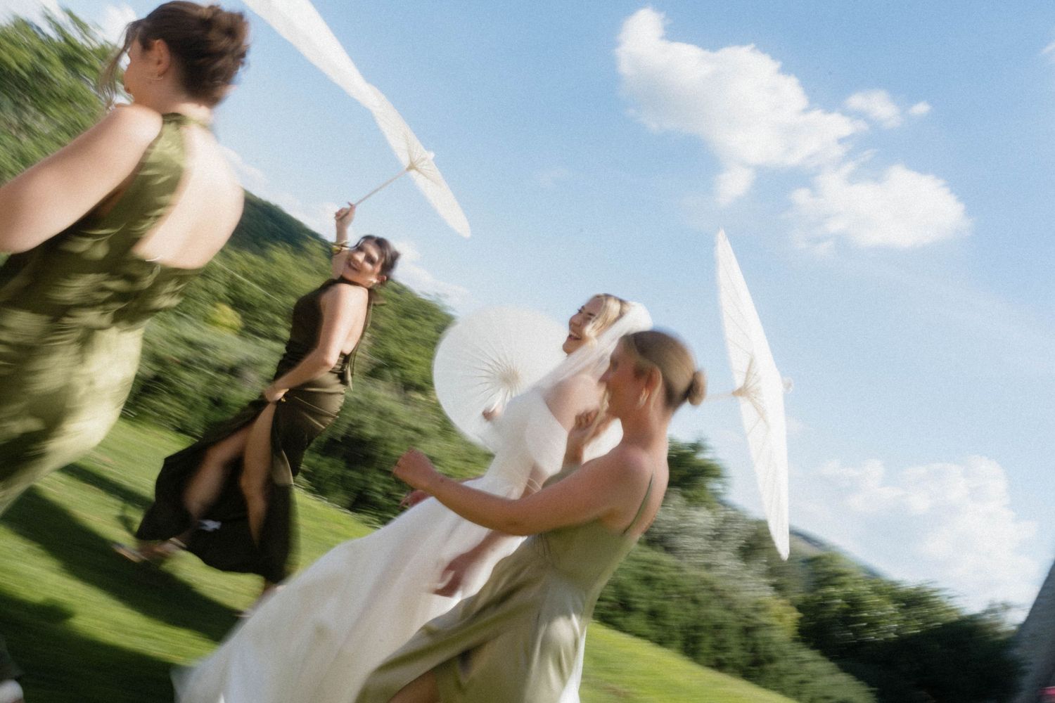 Motion-blur photo of bride and bridesmaids twirling with white parasols on a bright sunny wedding day.