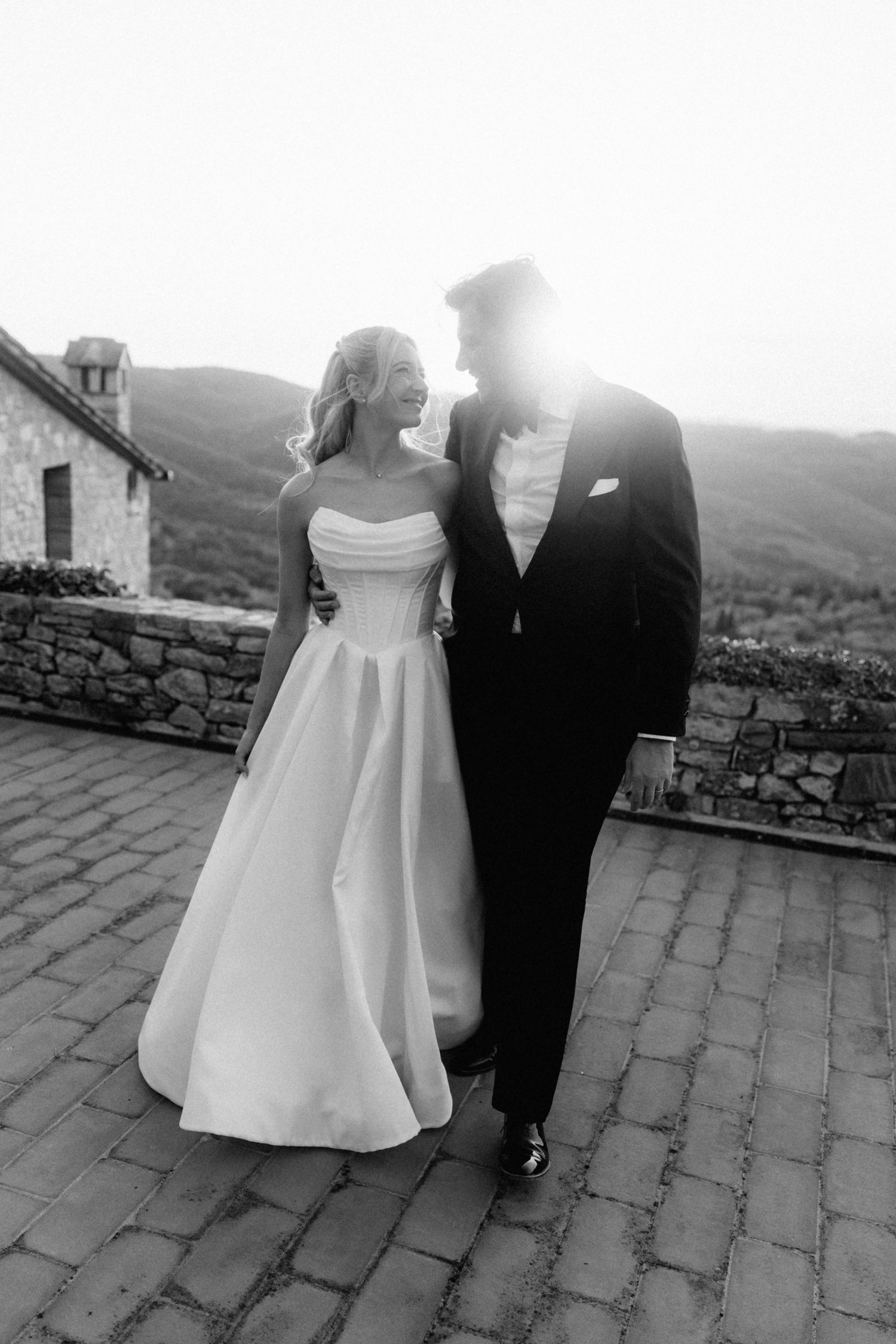 Black and white photo of a bride and groom sharing a romantic moment on a stone terrace.
