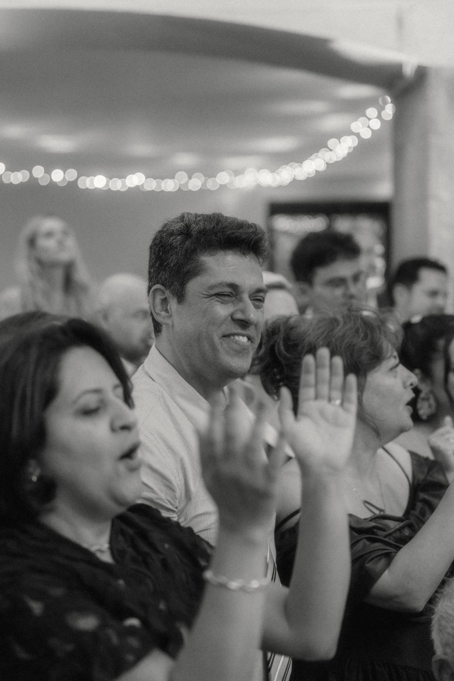 Black and white photo of joyful wedding guests clapping and celebrating at a reception.
