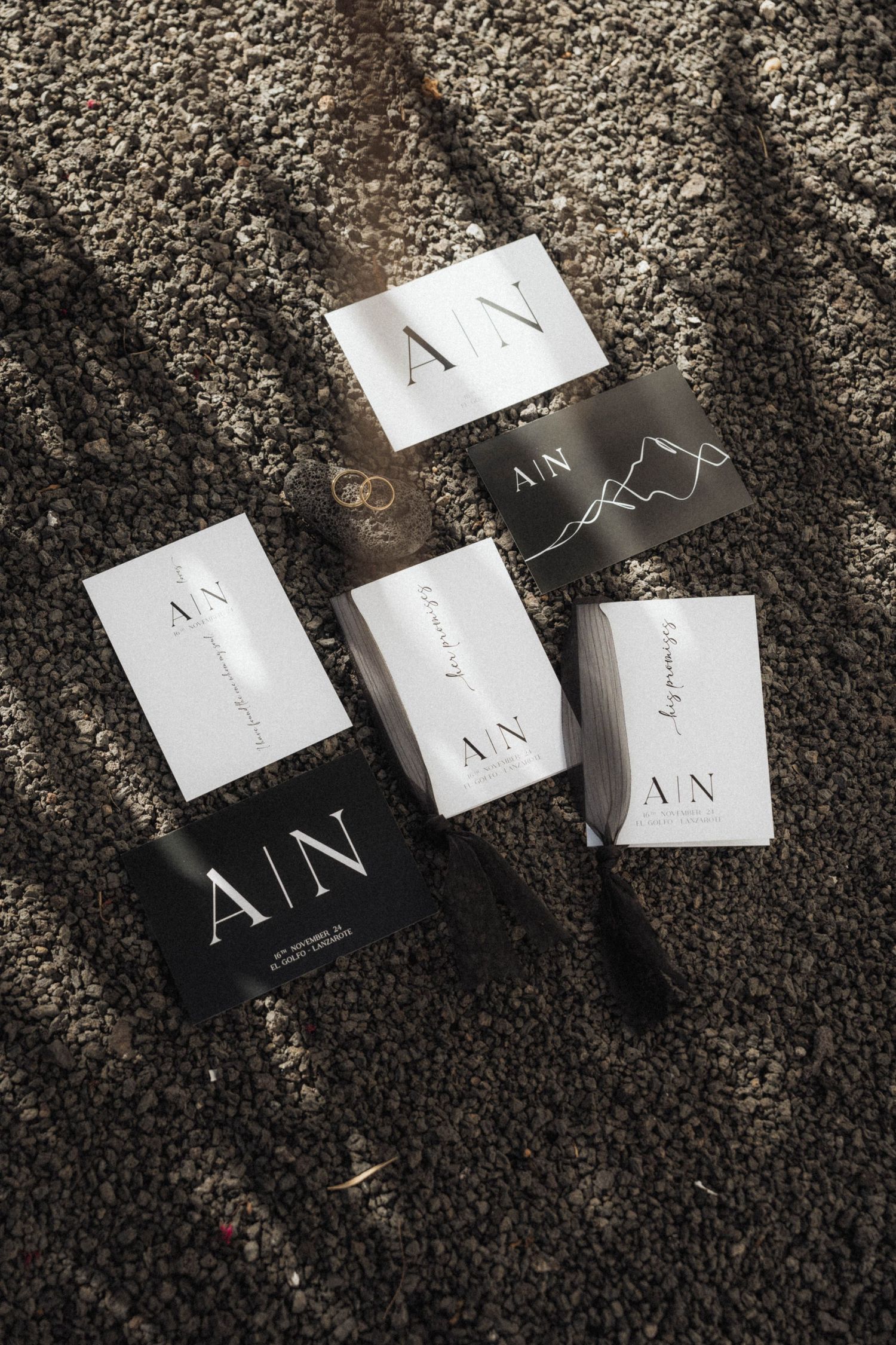 Elegant black and white wedding stationery suite with A/N monogram displayed on textured stone surface.