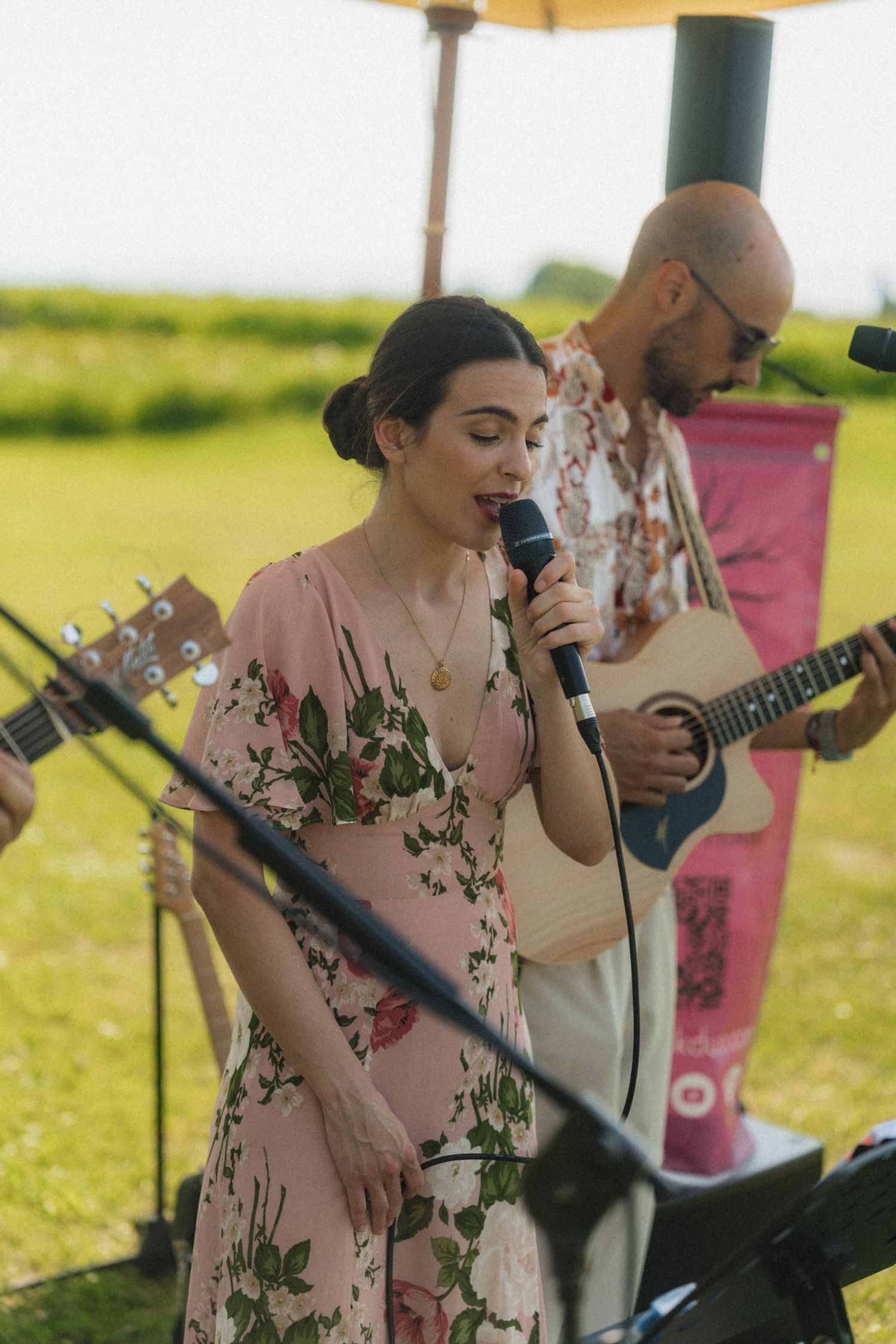 Female singer in floral dress performing with guitarist at outdoor wedding reception.