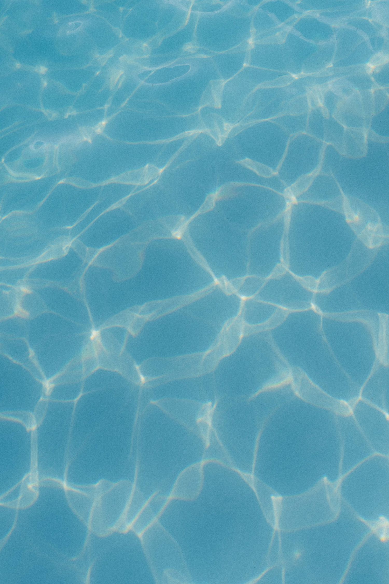 Close-up of clear blue swimming pool water with sunlight reflections creating rippling patterns on the surface.