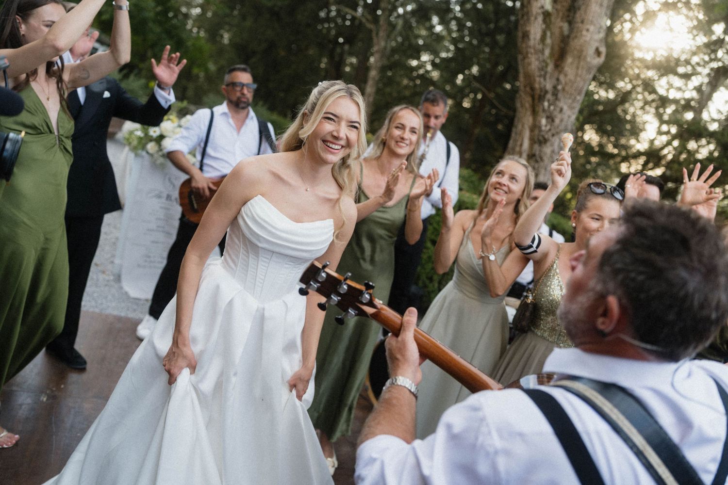 Joyful bride in strapless gown dancing with live guitarist at lively outdoor wedding celebration.