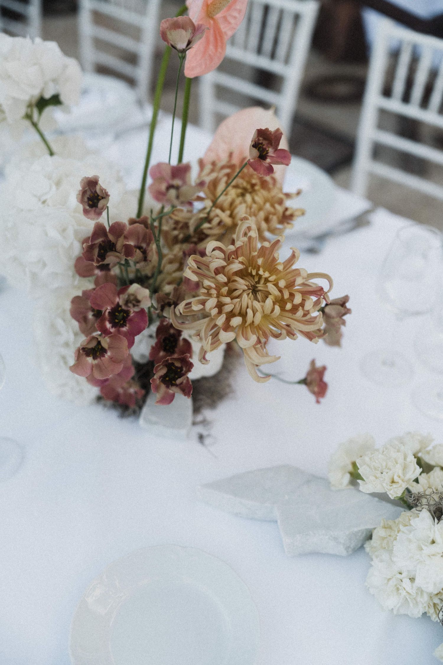 Elegant wedding table centerpiece with pink anthuriums, chrysanthemums and white flowers on white linen.