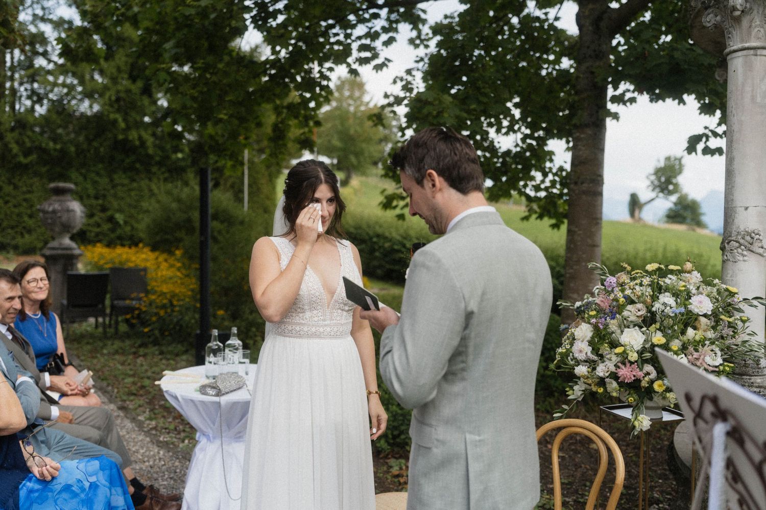 Emotional bride wiping tears while groom reads vows during an intimate outdoor wedding ceremony.