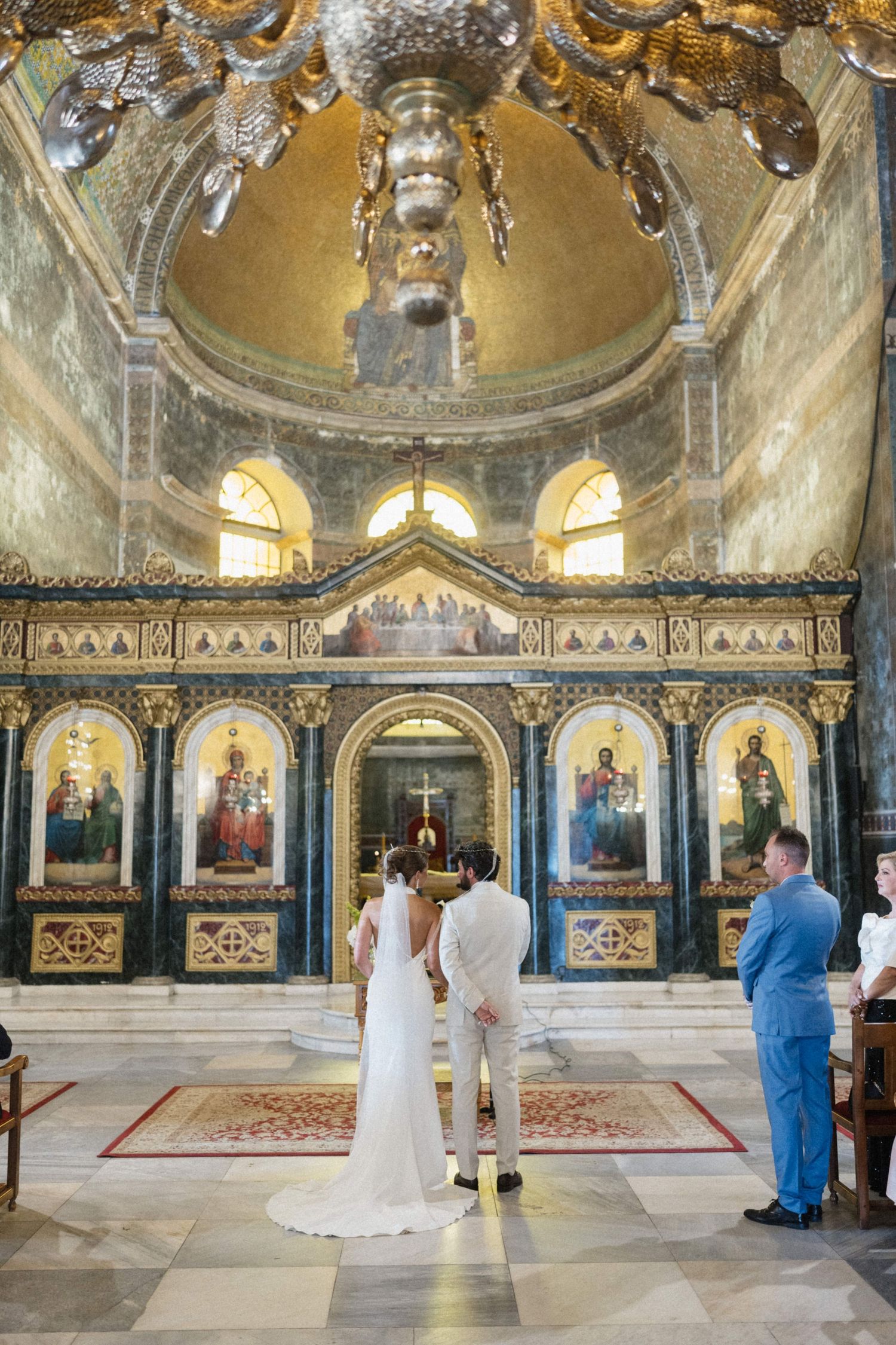 Bride and groom stand at ornate Orthodox church altar with golden dome and iconic mosaics.