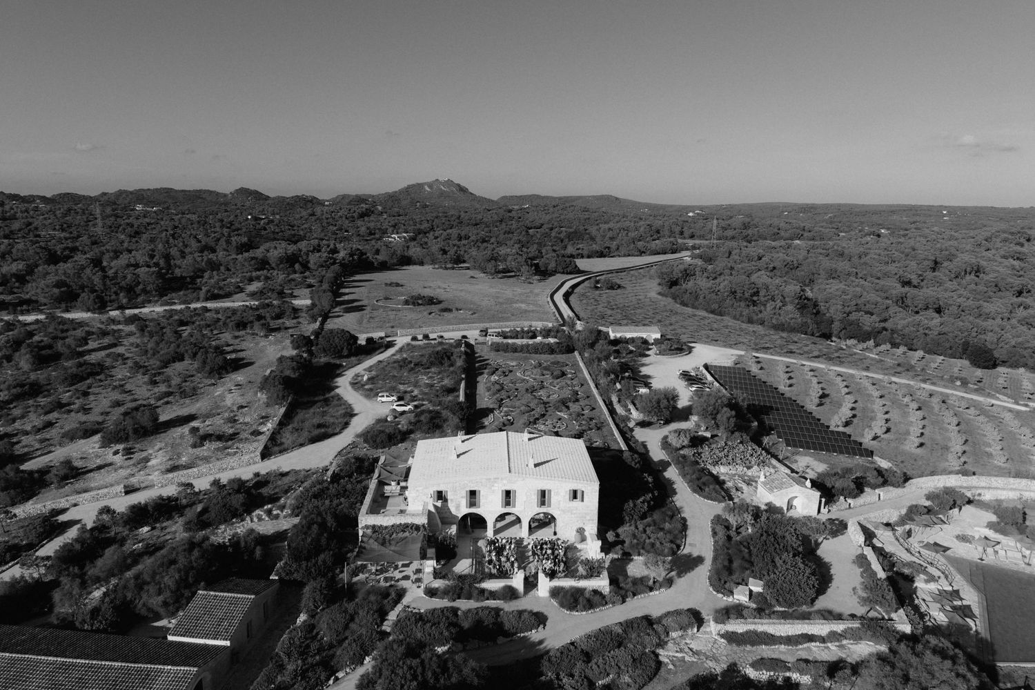 Black and white aerial view of a rustic countryside wedding estate surrounded by olive groves, vineyards and rolling hills.