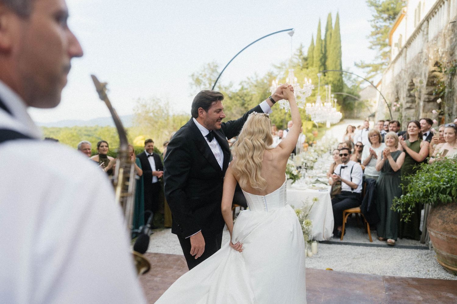 Bride and groom celebrating first dance at outdoor Italian villa wedding with cheering guests.