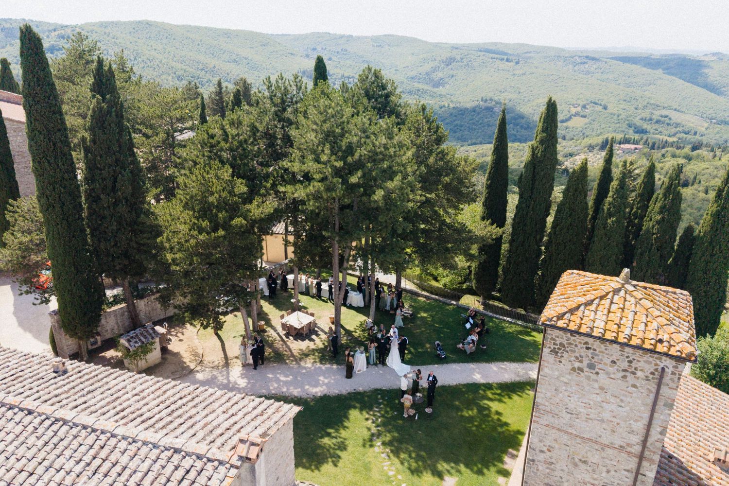 Aerial view of an outdoor wedding ceremony surrounded by cypress trees with rolling Tuscan hills.